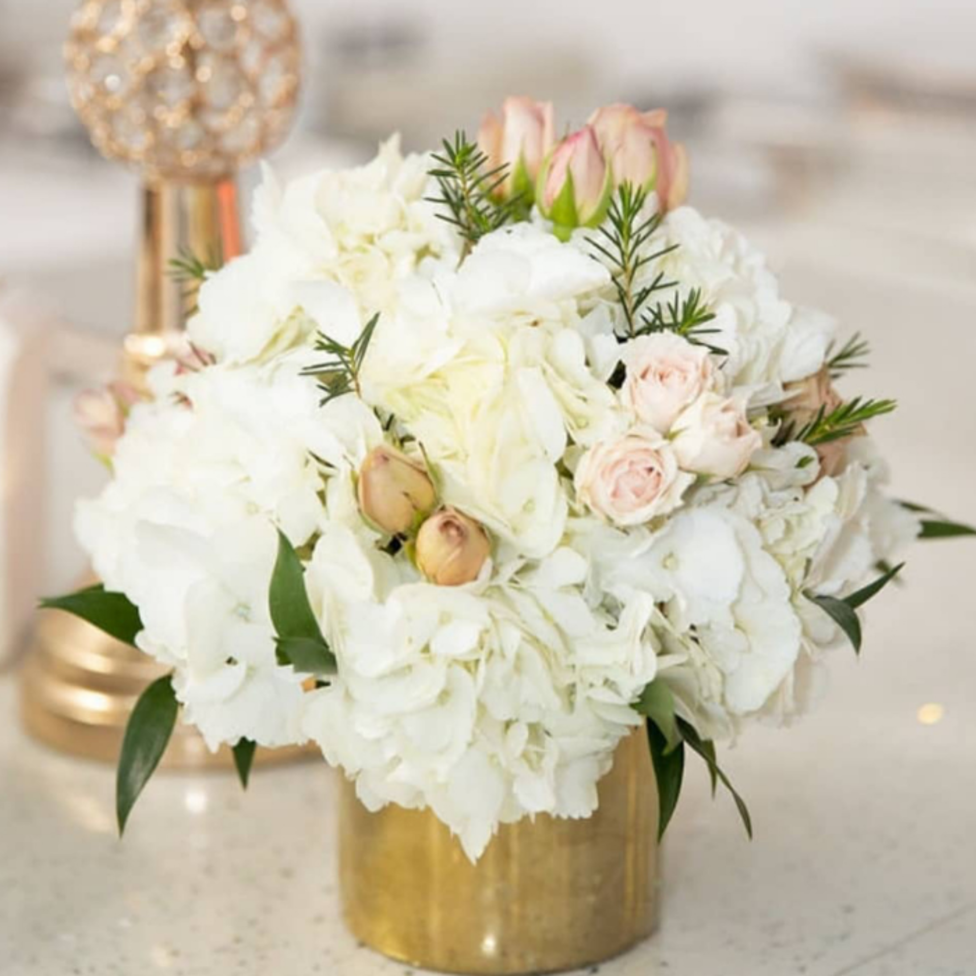 Sophisticated floral centerpiece of white hydrangeas and pink roses in a gold vase with greenery