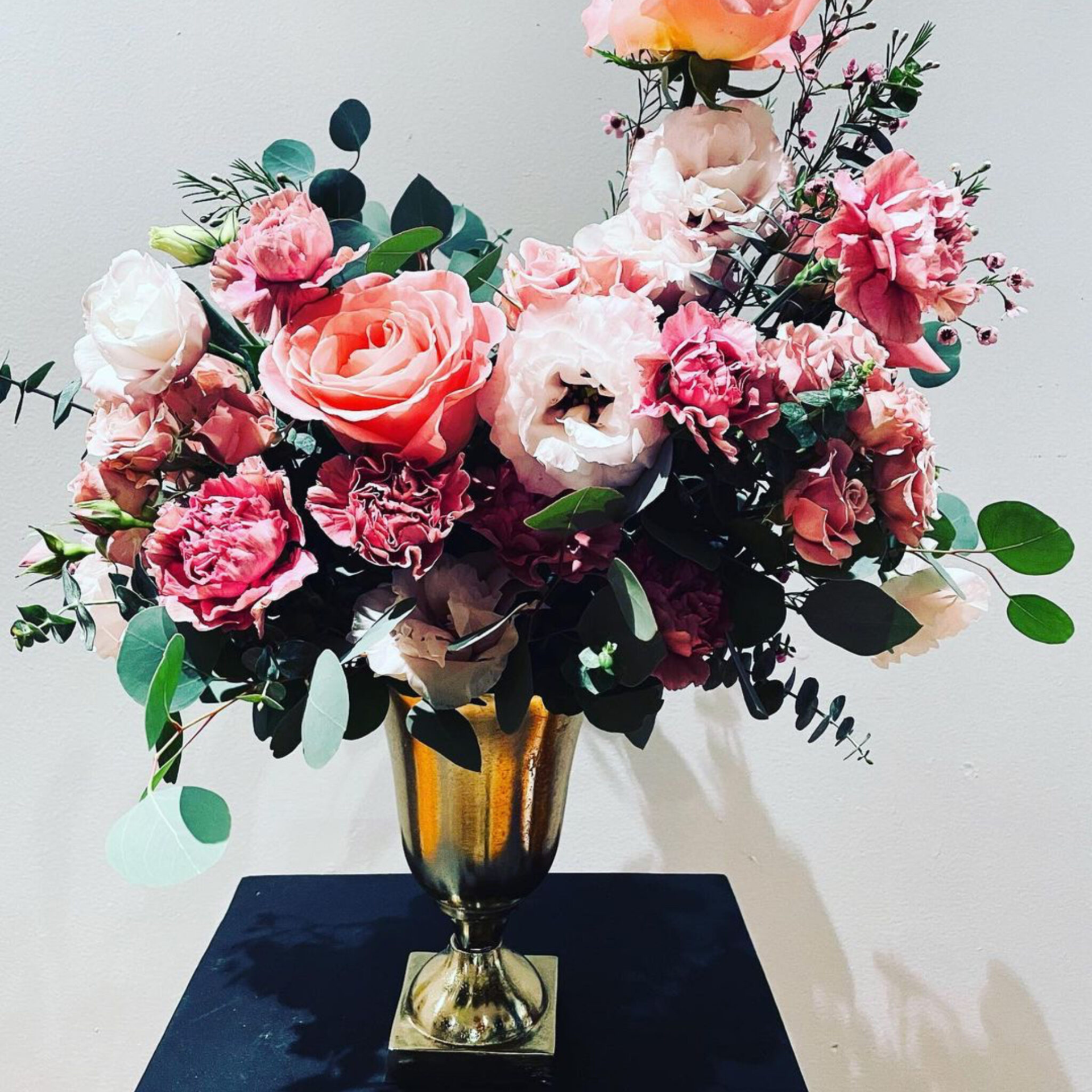 Elegant floral arrangement of pink roses, carnations, and lisianthus in a gold vase with eucalyptus leaves