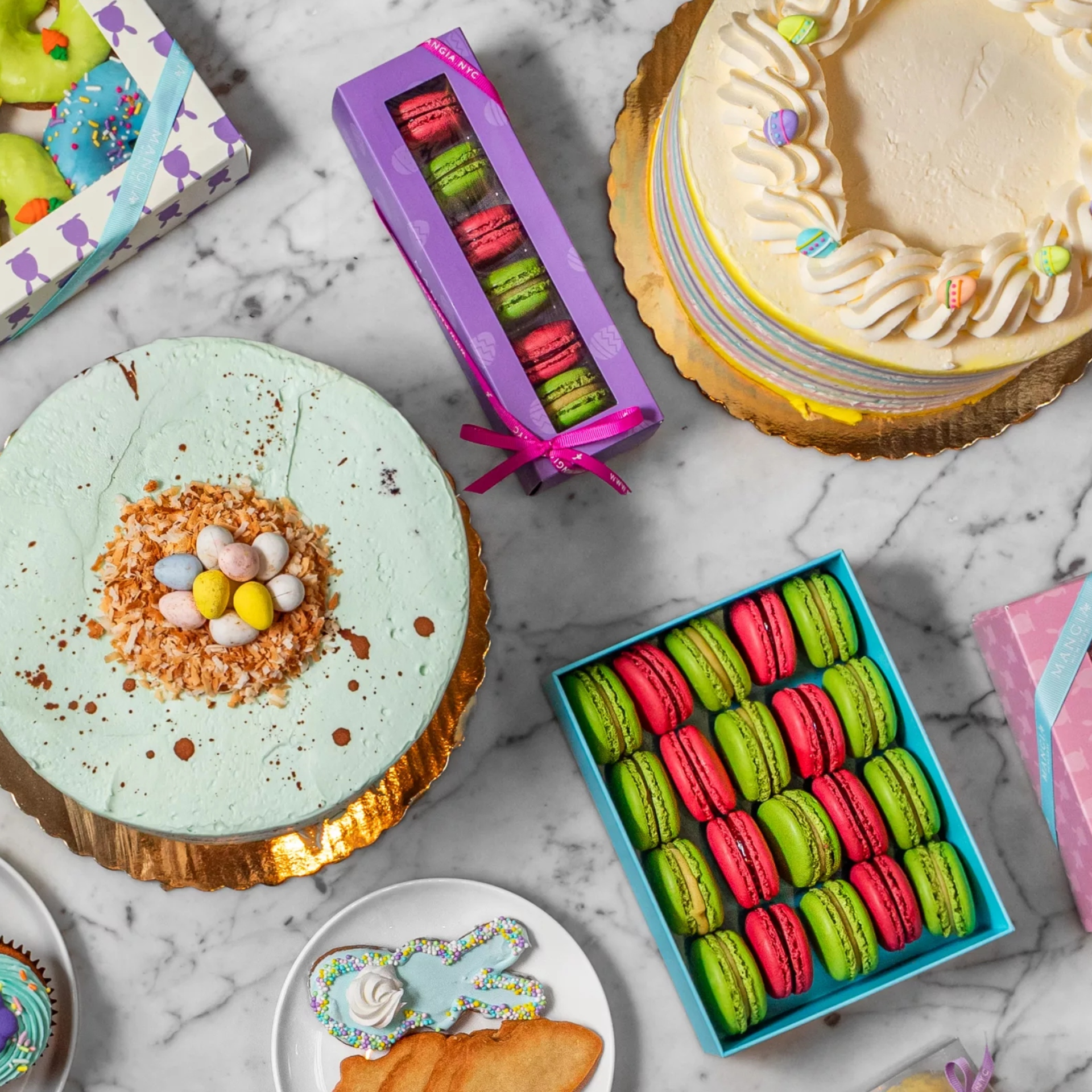 Colorful assortment of Easter-themed cakes, macarons, and cookies displayed on a marble surface