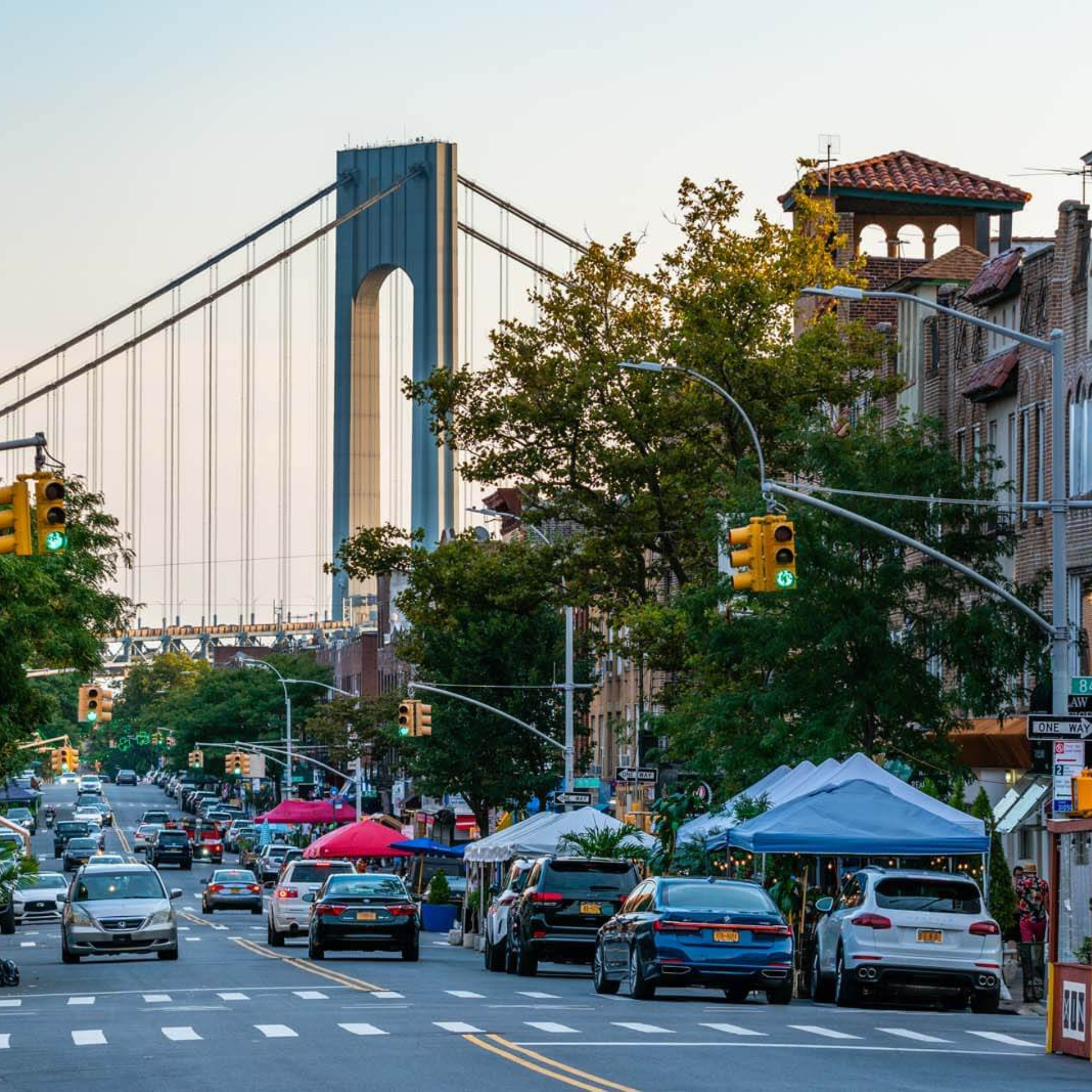 Busy city street with tents and cars, suspension bridge in the background