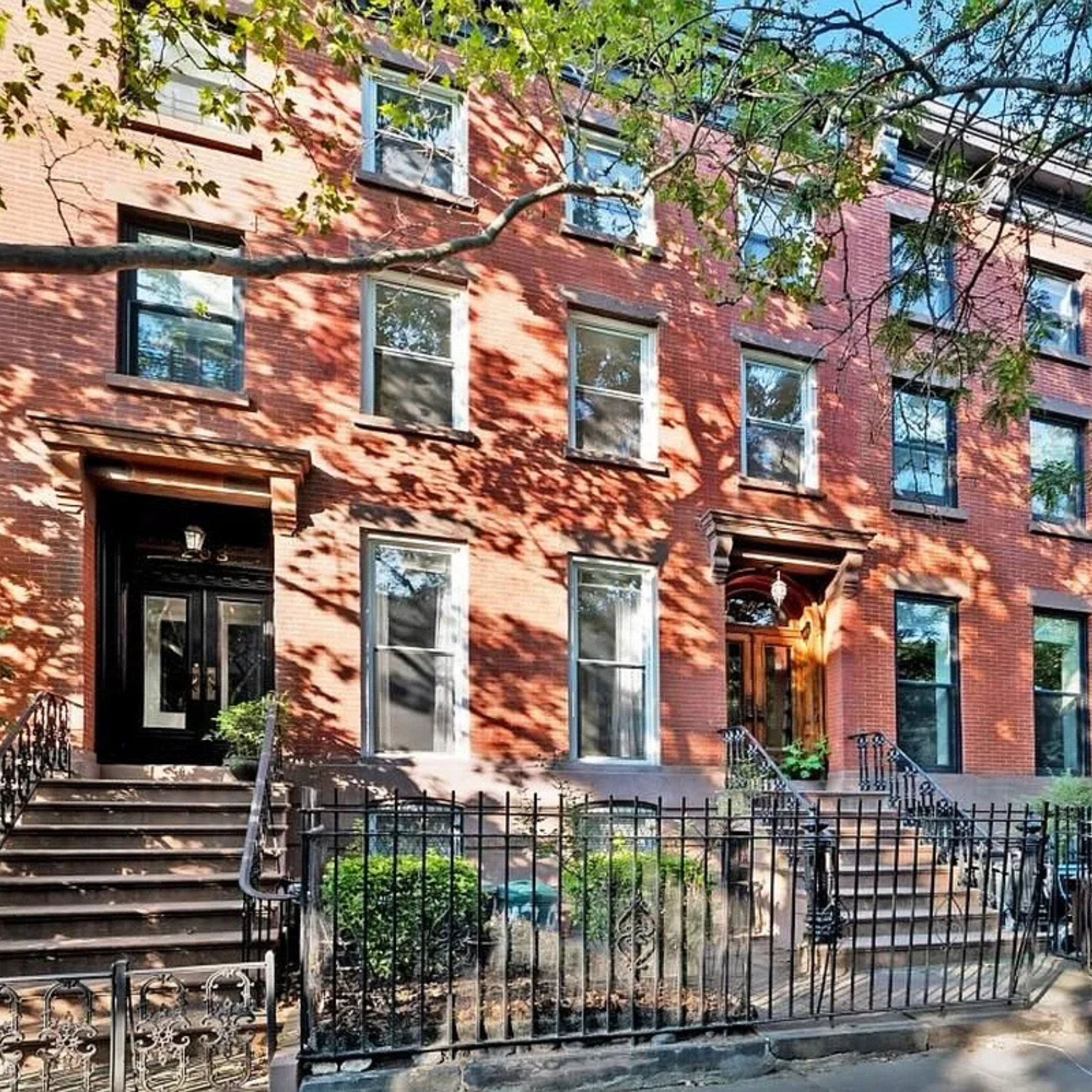 Row of red brick brownstone townhouses with stoops, iron railings, and shaded tree-lined facade