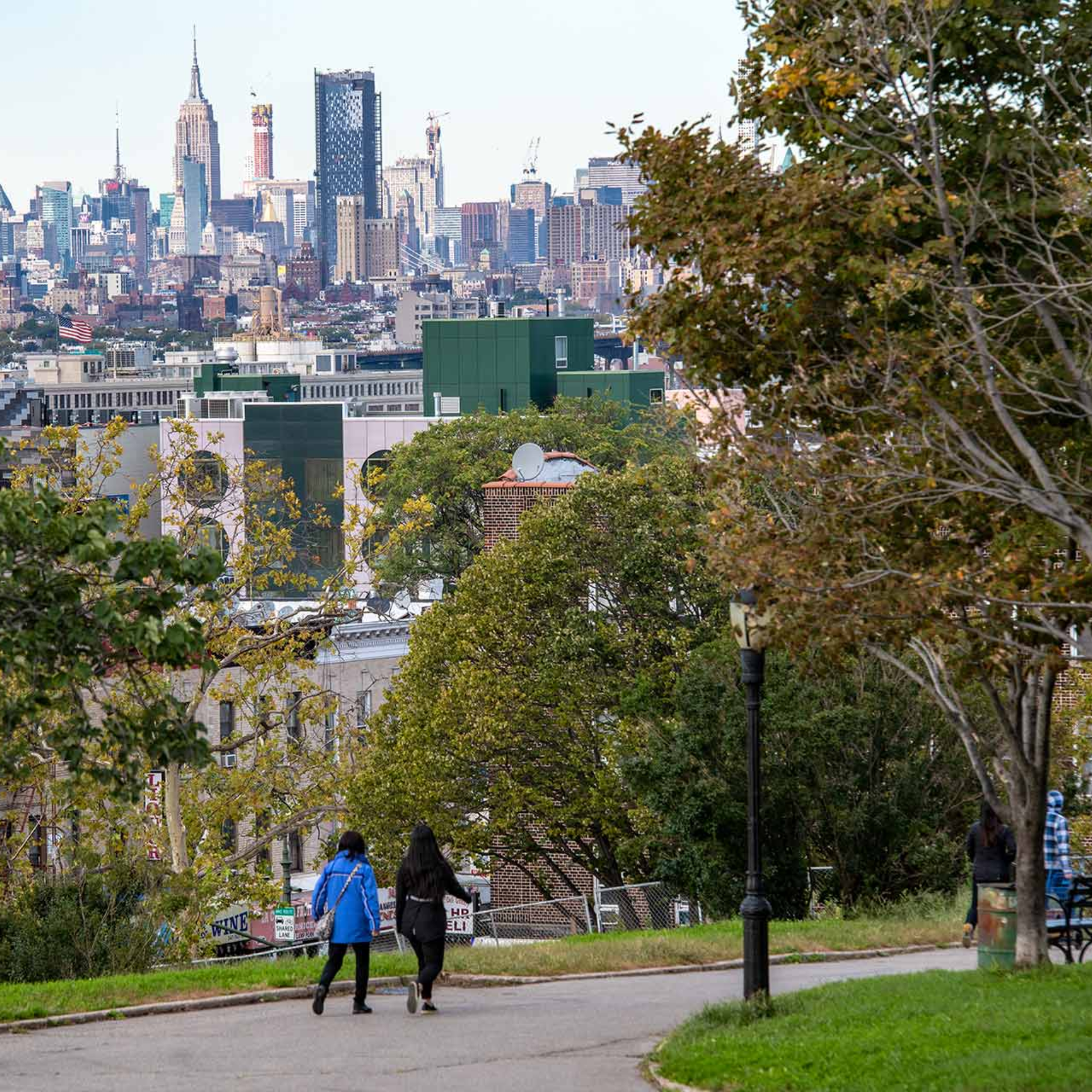 Park walkway overlooking a city skyline with people walking among autumn trees