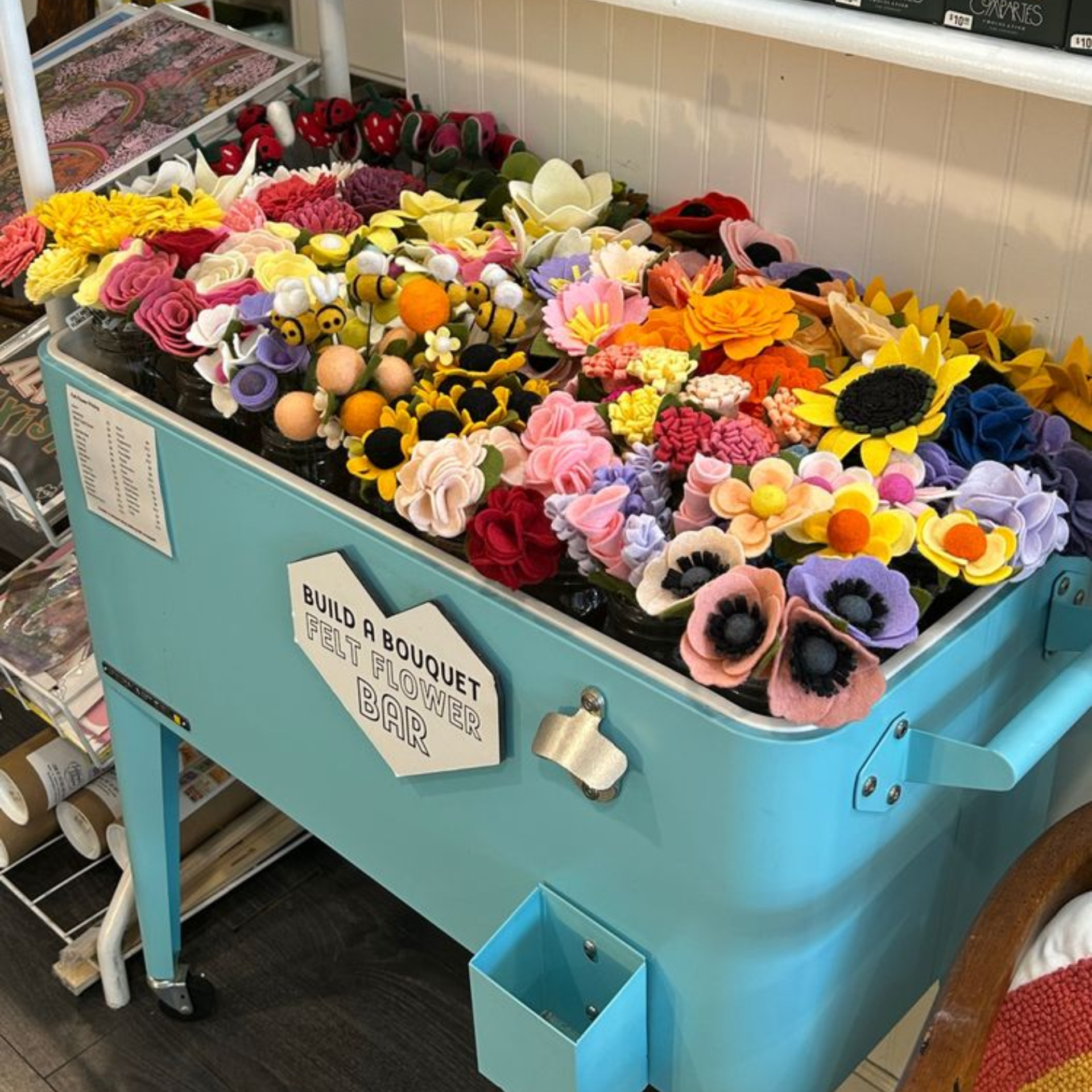 Light blue cart labeled Build a Bouquet Felt Flower Bar filled with colorful felt flowers and decorations
