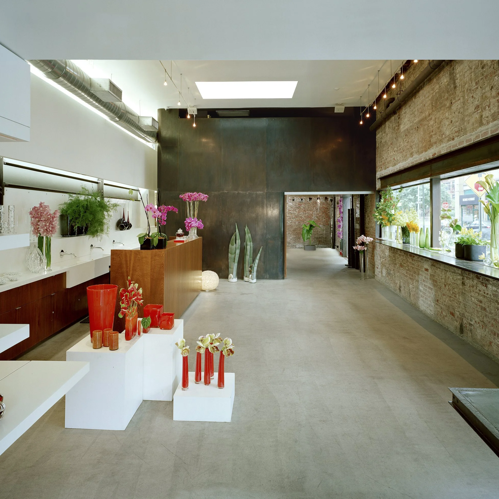 Modern flower shop with exposed brick, concrete floor, and floral displays on counters and pedestals