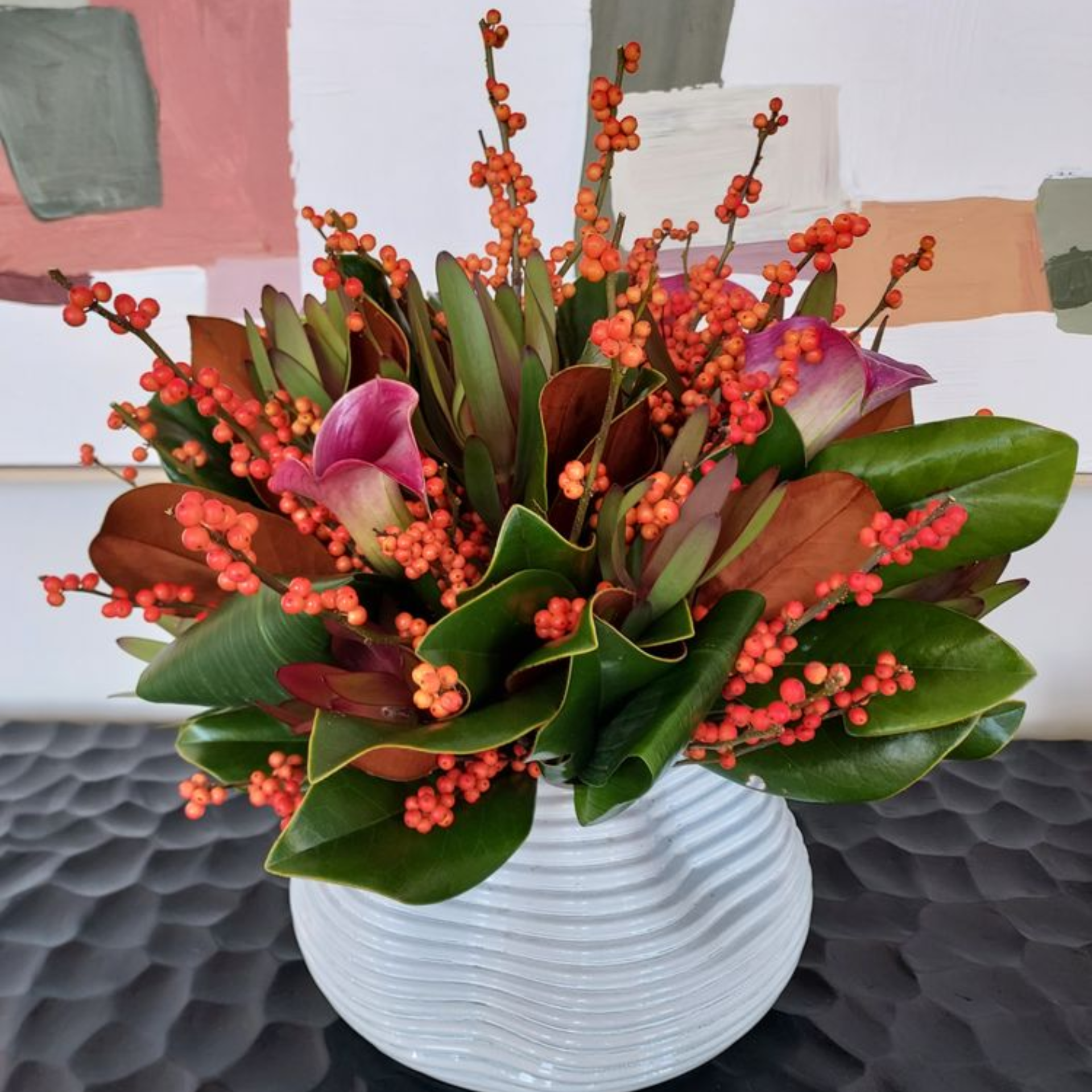 Floral arrangement in white vase with green leaves, orange berries, and purple calla lilies