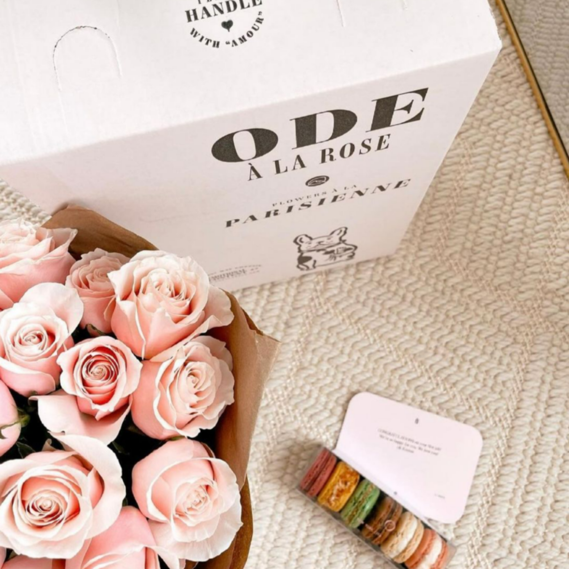 Bouquet of pink roses with gift box labeled Ode à la Rose and package of colorful macarons