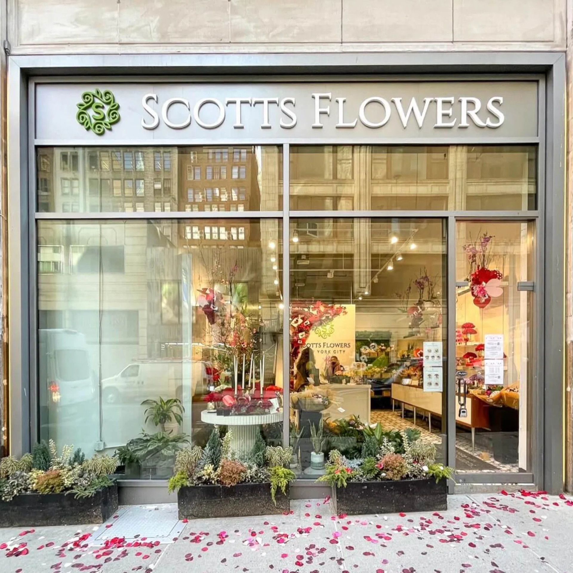 Flower shop storefront with large glass windows, floral displays, and sign reading Scotts Flowers