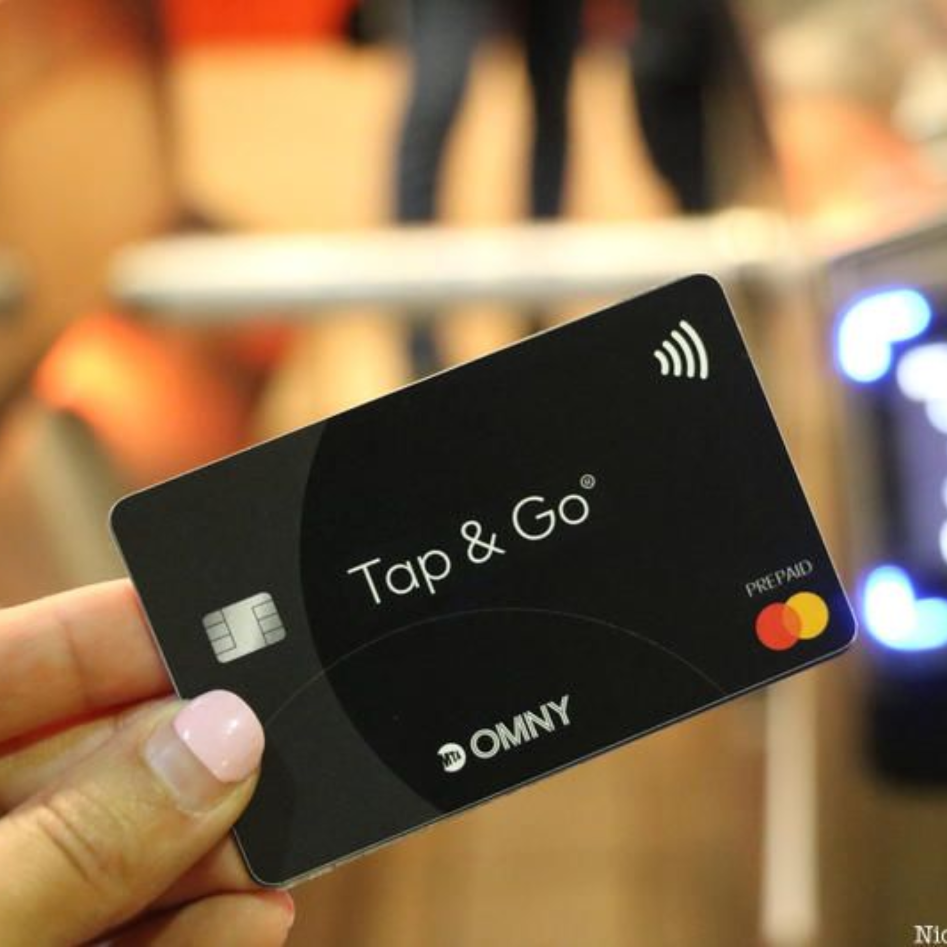 Hand holding black “Tap & Go” OMNY Mastercard contactless card near transit terminal
