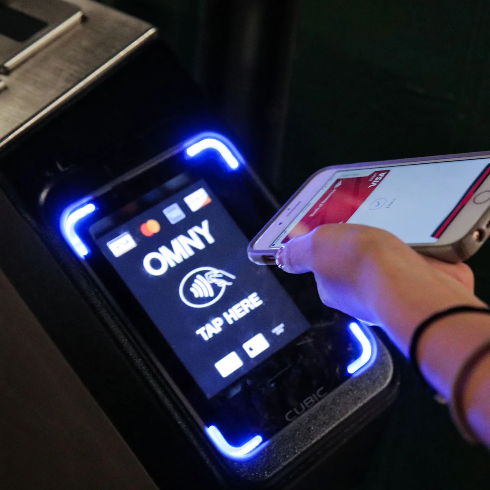 Person tapping smartphone on OMNY contactless payment terminal with Visa and Mastercard logos