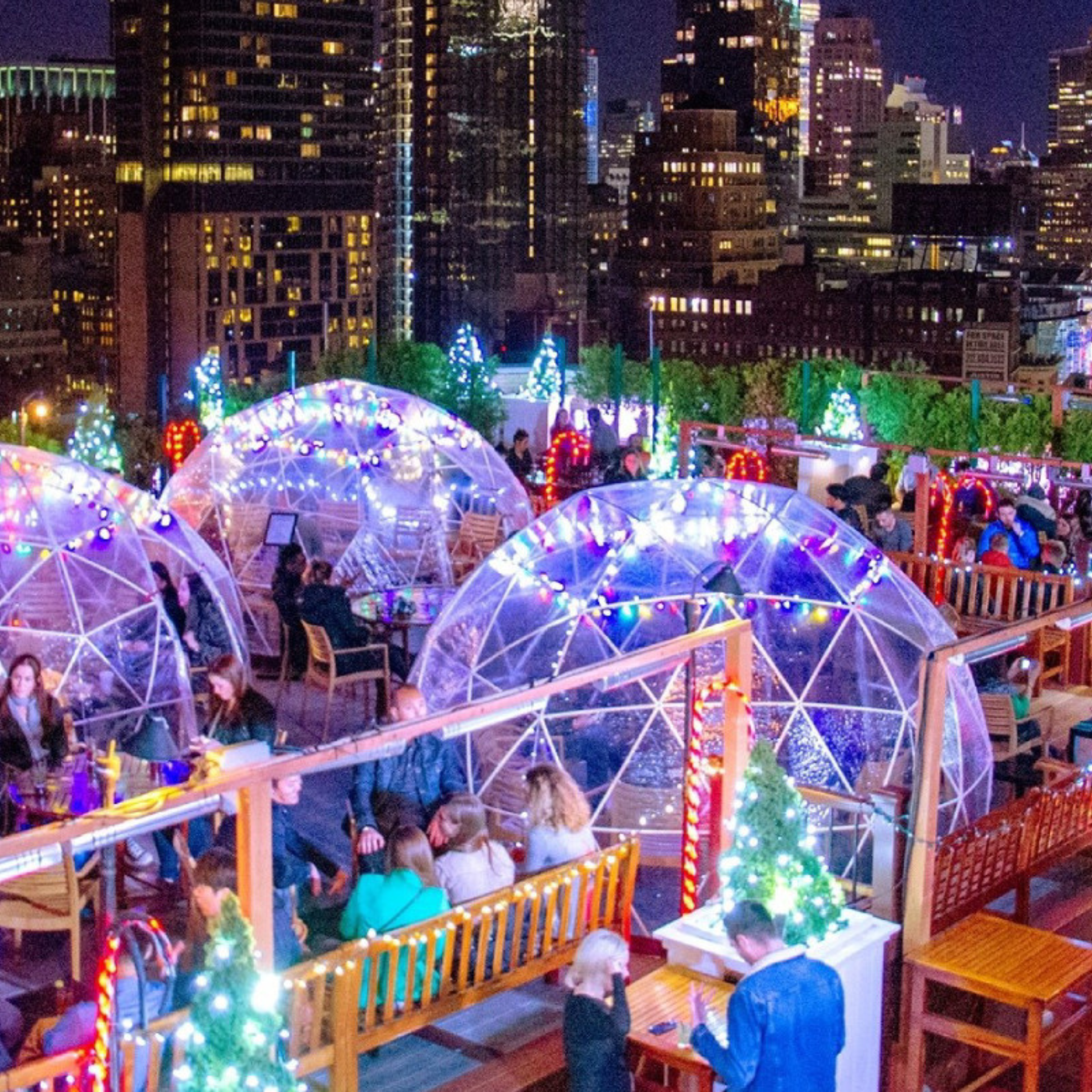 Festive rooftop dining scene with geodesic domes, holiday lights, and city skyscrapers at night