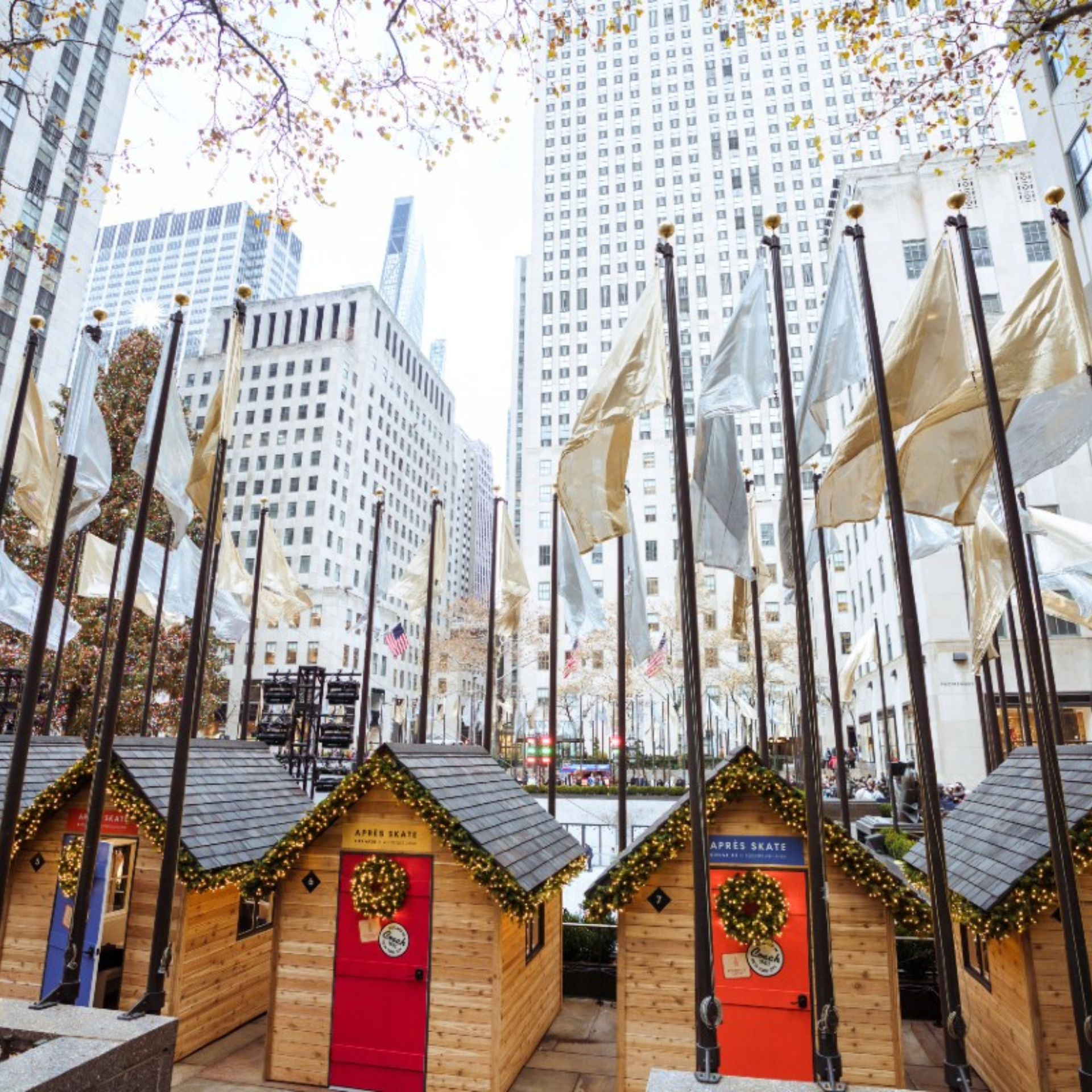 Holiday huts labeled “APRÈS SKATE” at Rockefeller Center, decorated with garlands and festive lights