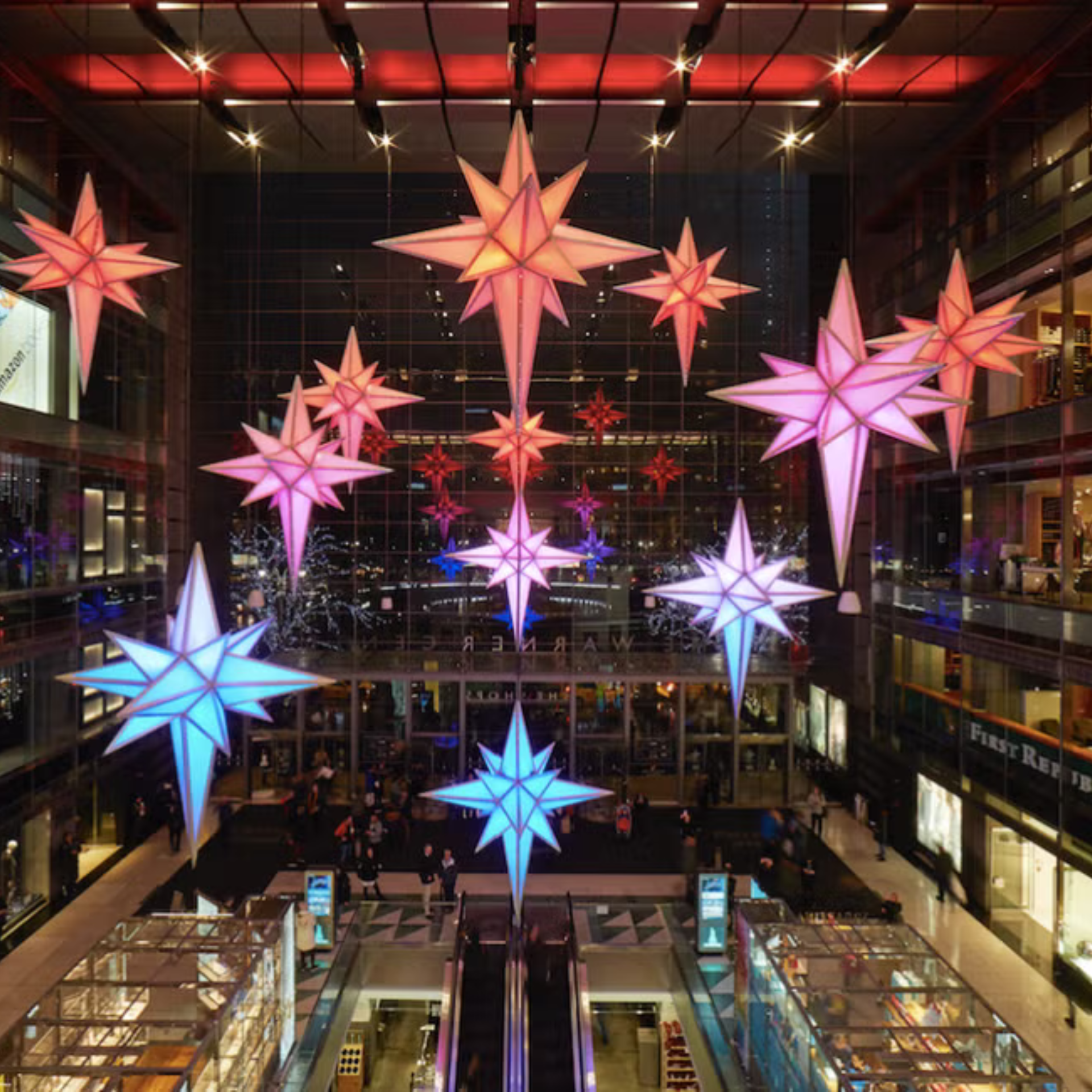 Indoor holiday display with colorful illuminated star decorations hanging above a busy shopping area