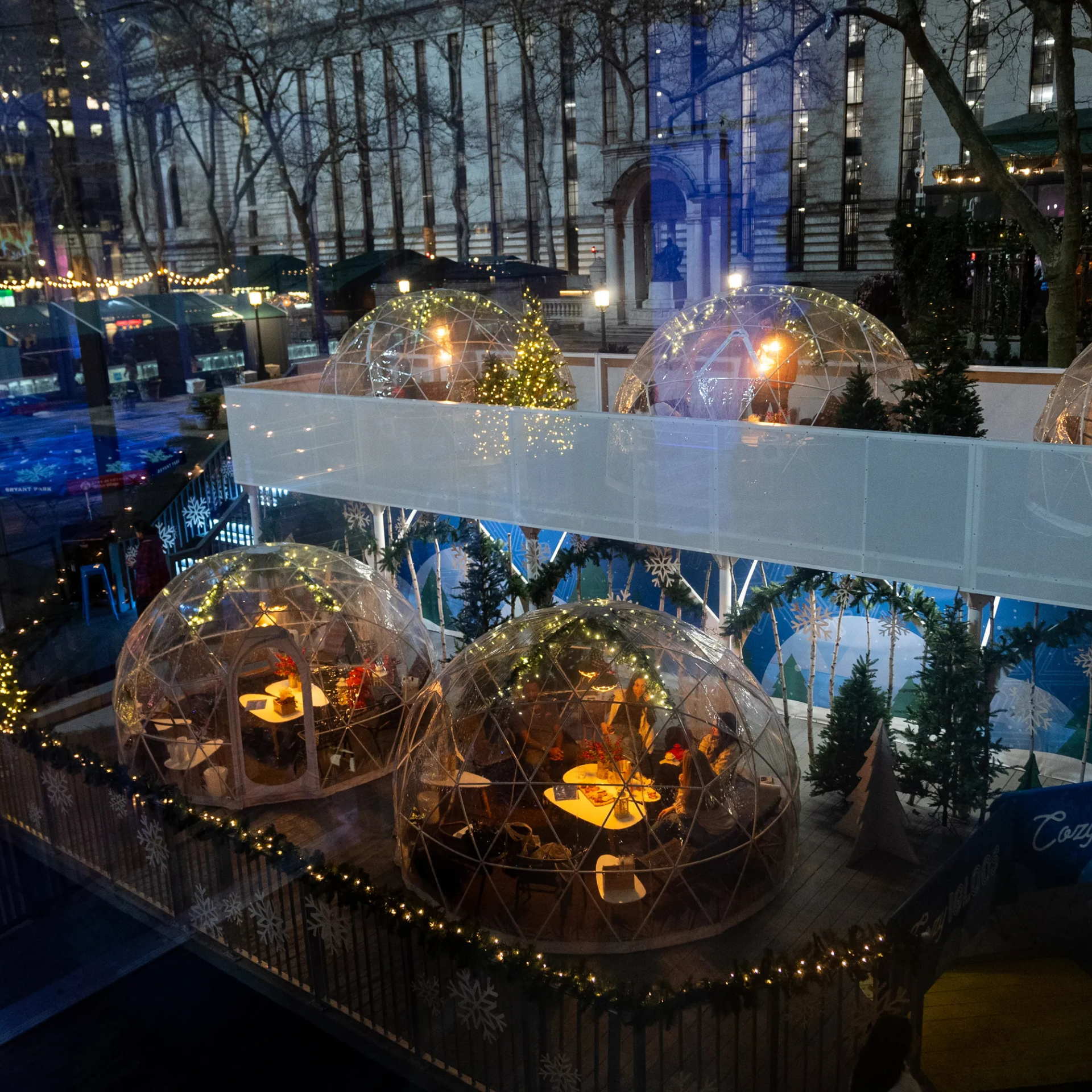 Outdoor holiday dining setup with lit geodesic domes, festive trees, and classical city architecture