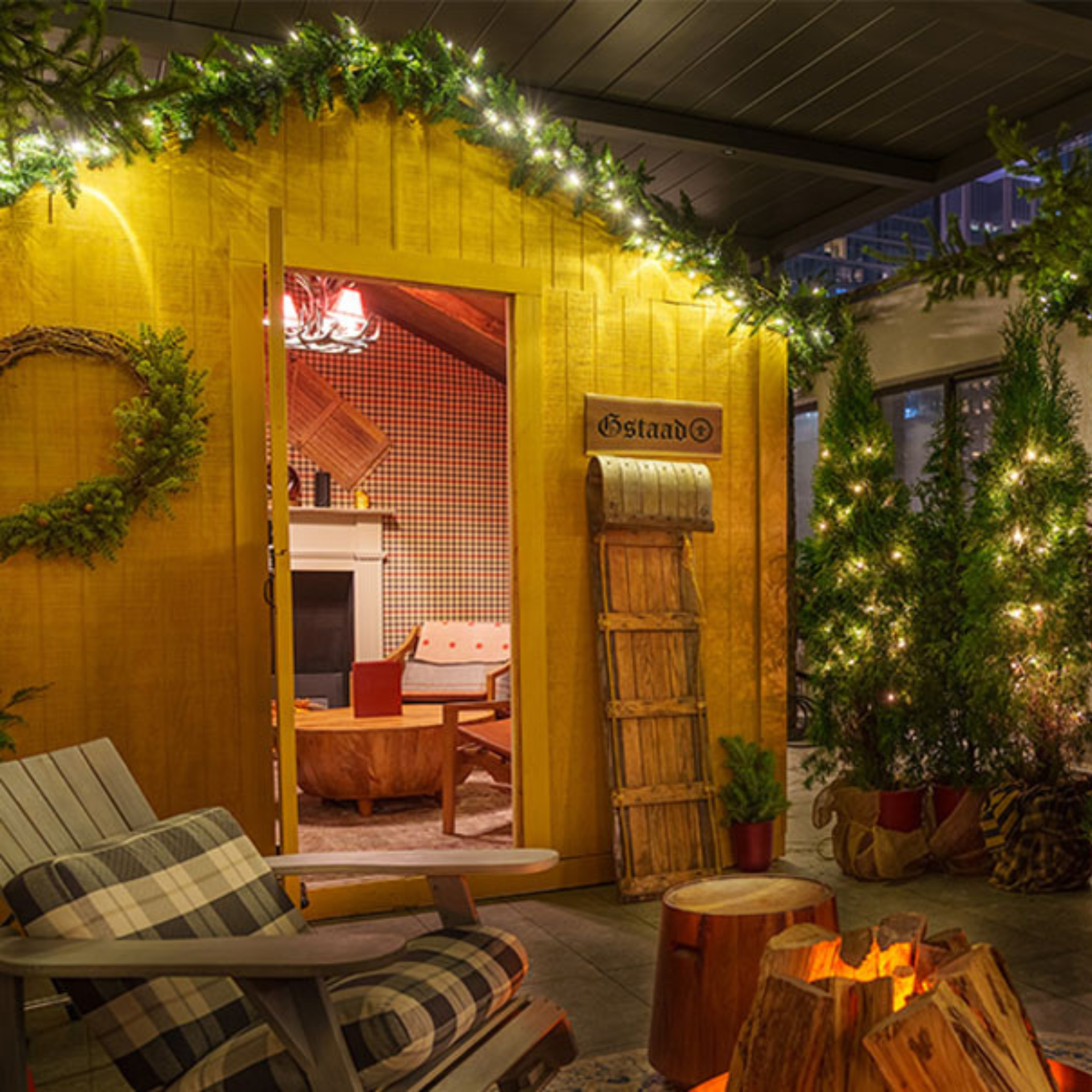 Festive outdoor cabin scene with pine garlands, string lights, and cozy seating around a faux fire pit