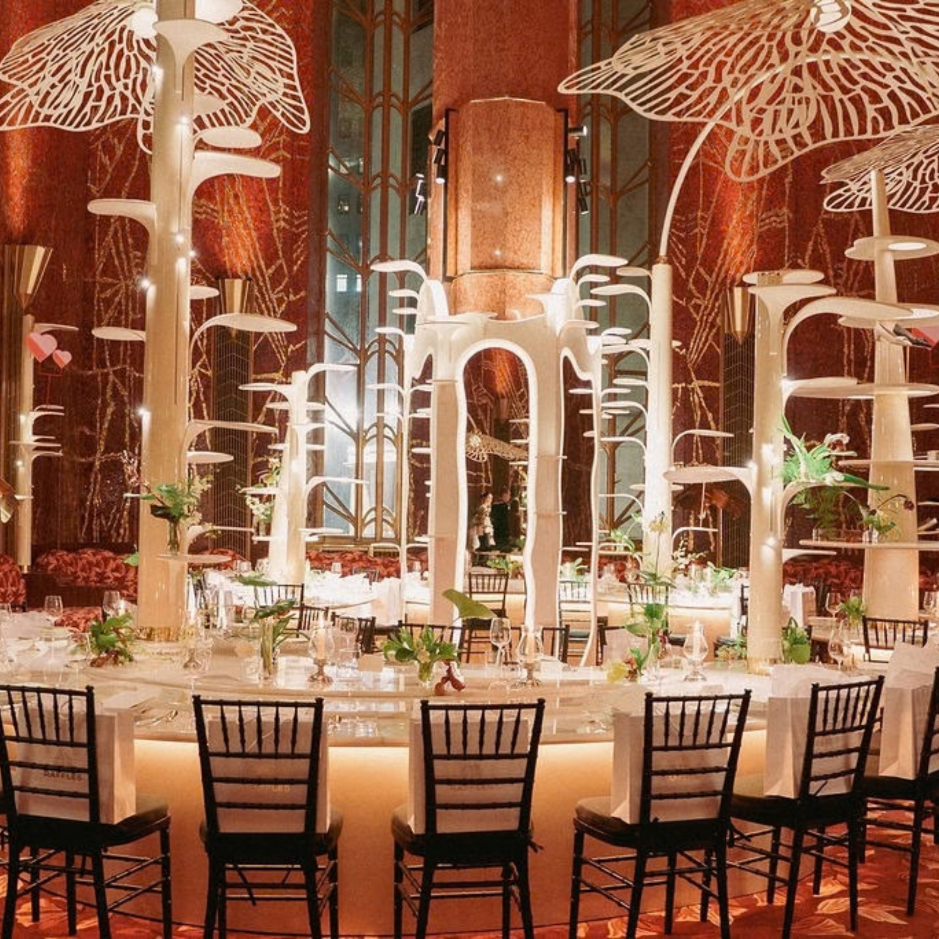 Luxurious dining room with curved table, floral centerpieces, and sculptural illuminated installations