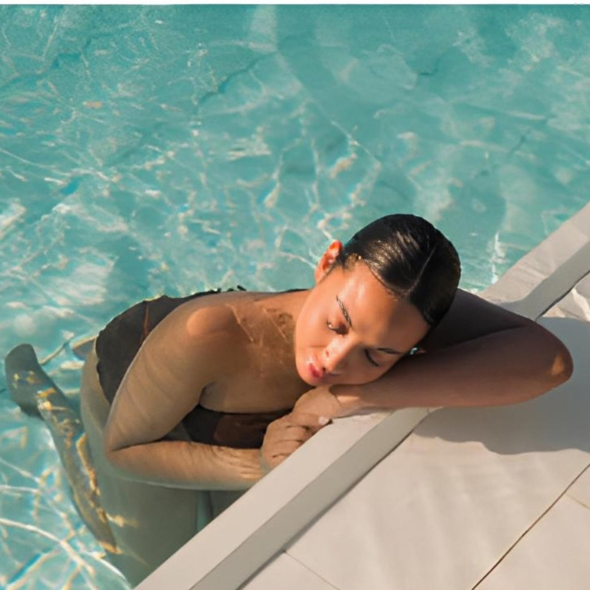 Person in swimming pool resting head on arm at pool edge, eyes closed in sunlight