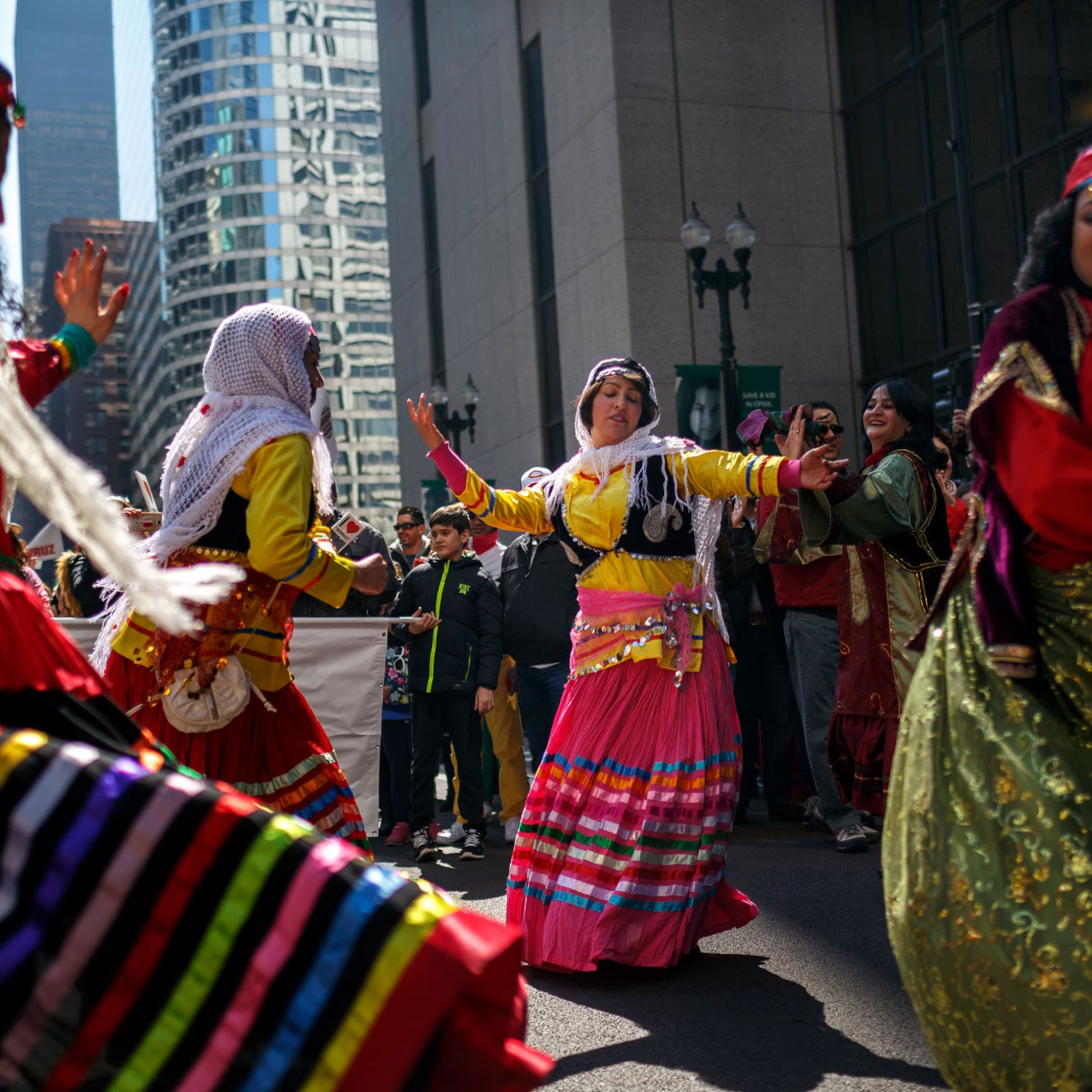 Street festival with dancers in vibrant traditional costumes performing in front of tall city buildings
