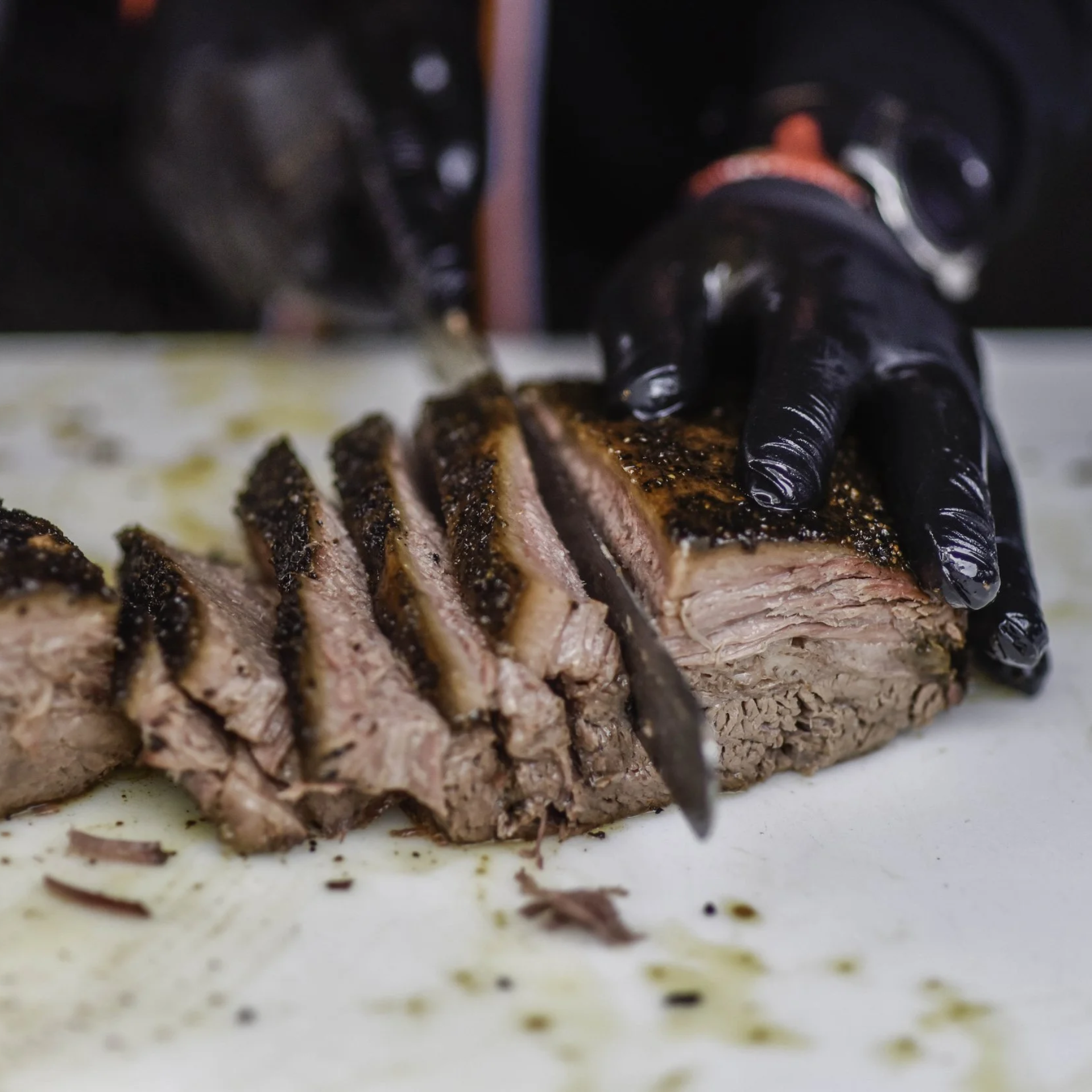 Close-up of gloved hands slicing juicy brisket with a knife on a cutting board