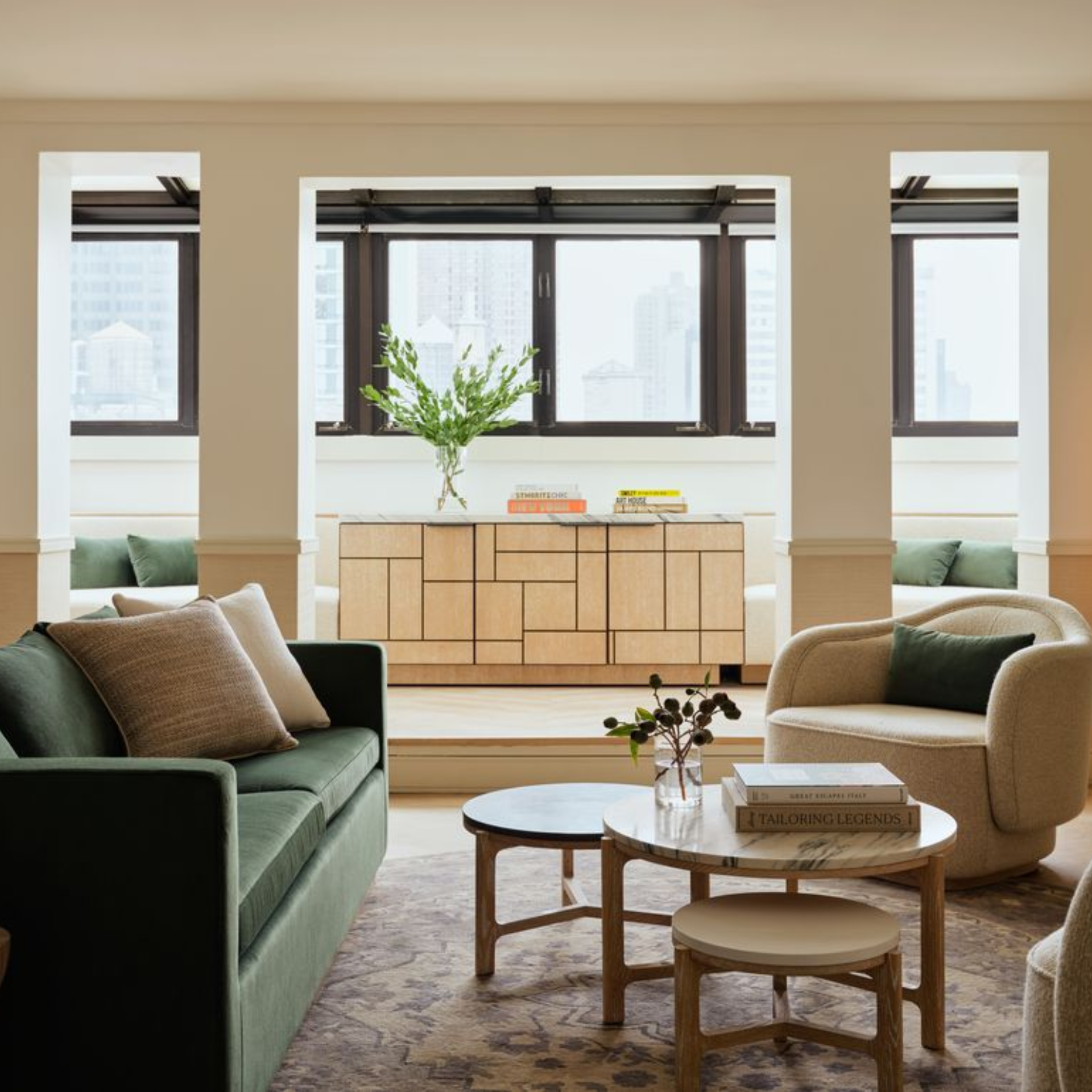 Modern living room with green sofa, beige armchair, marble coffee tables, and city view through large windows