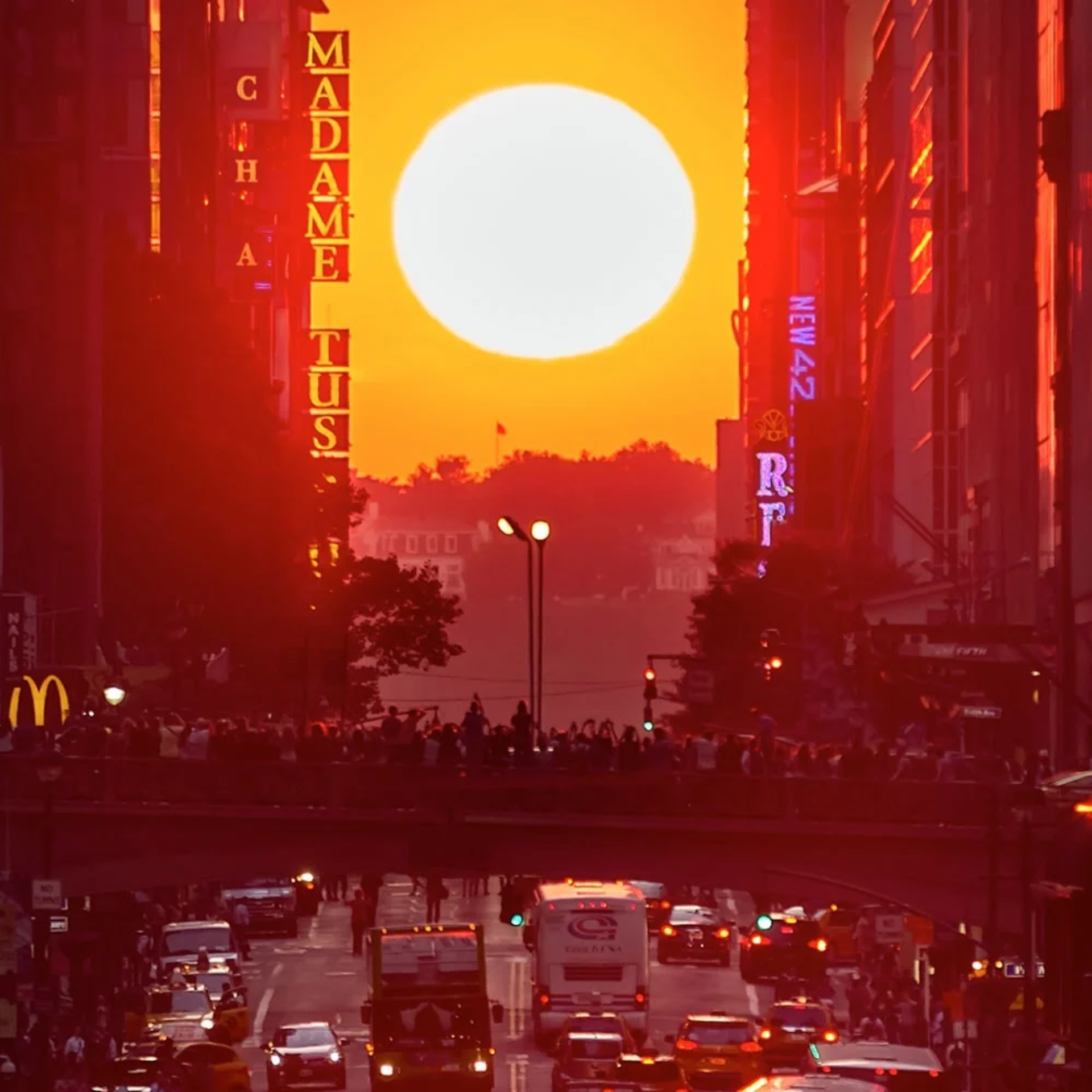 Sunset aligns between tall buildings on a busy New York street, glowing orange with crowds and traffic