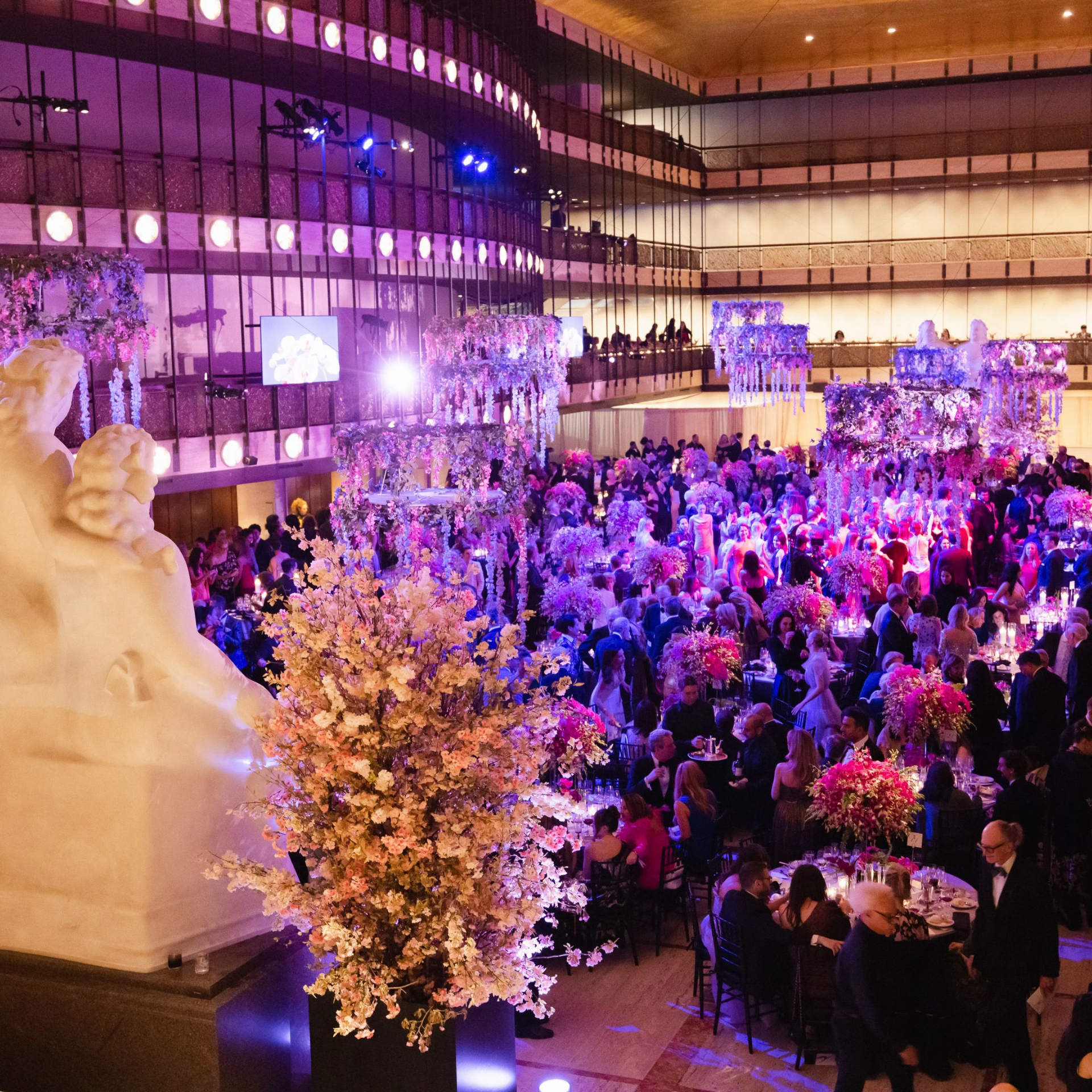 Lavish gala in a grand hall with floral décor, round tables, and guests in formal attire