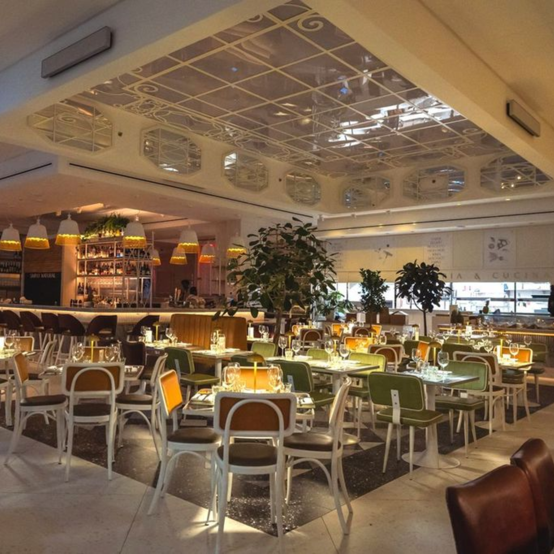 Modern restaurant interior with warm lighting, geometric ceiling design, and tables set for dining