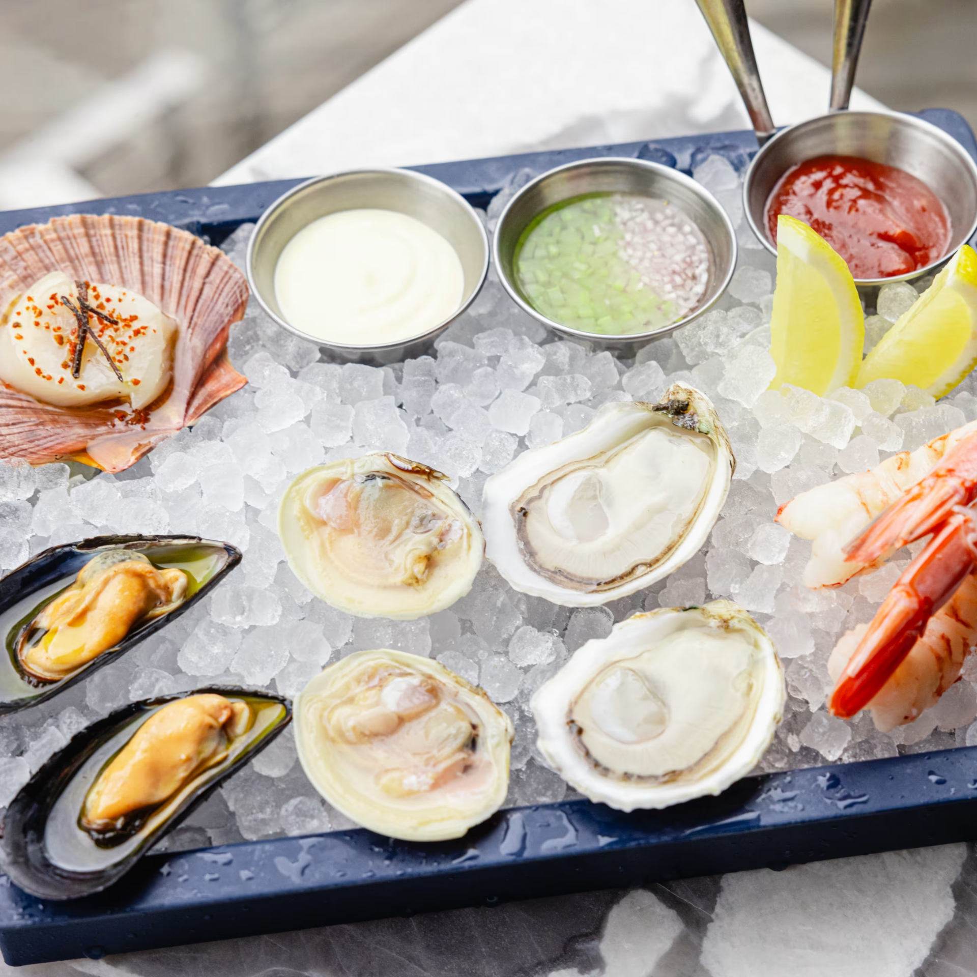 Seafood platter on ice with oysters, clams, mussels, shrimp, scallop, sauces, and lemon wedges, NYC dining delicacy featured in daily things to do in NYC any day