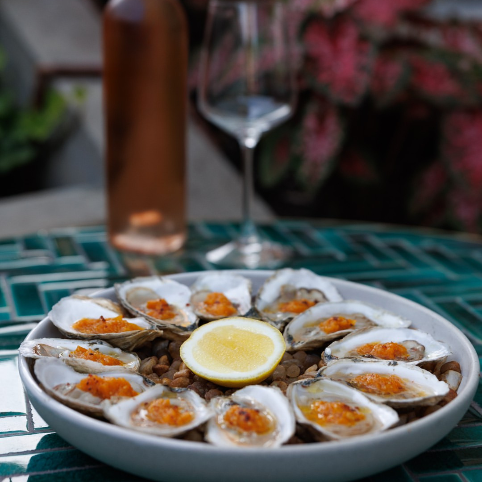Plate of oysters with orange garnish on lentils, lemon half, rosé wine bottle and glass on green‑tiled table, refined NYC seafood dining featured in daily things to do in NYC any day