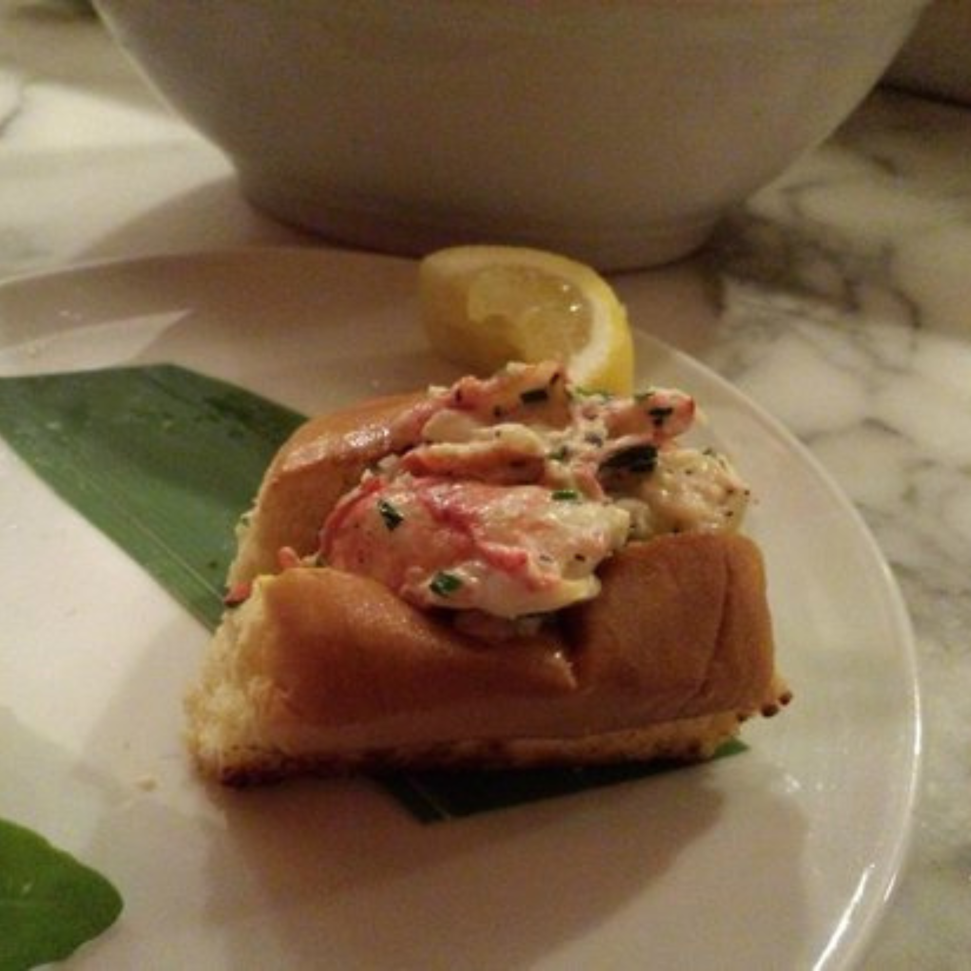 Small lobster roll on plate with lemon wedge