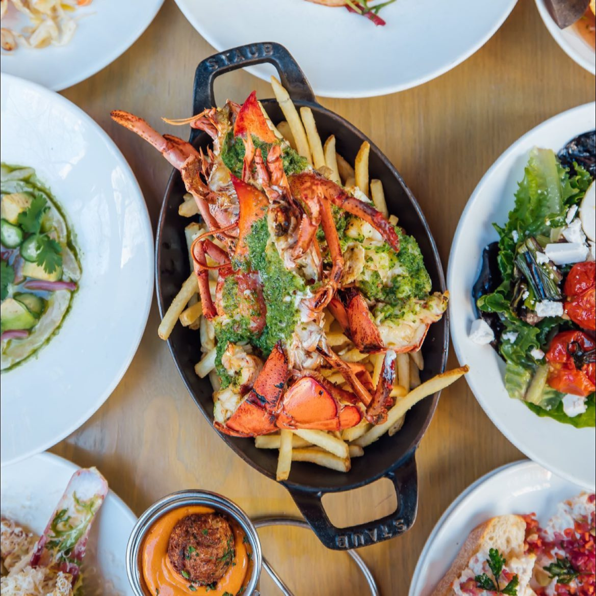 Lobster with fries in herb sauce, surrounded by side dishes