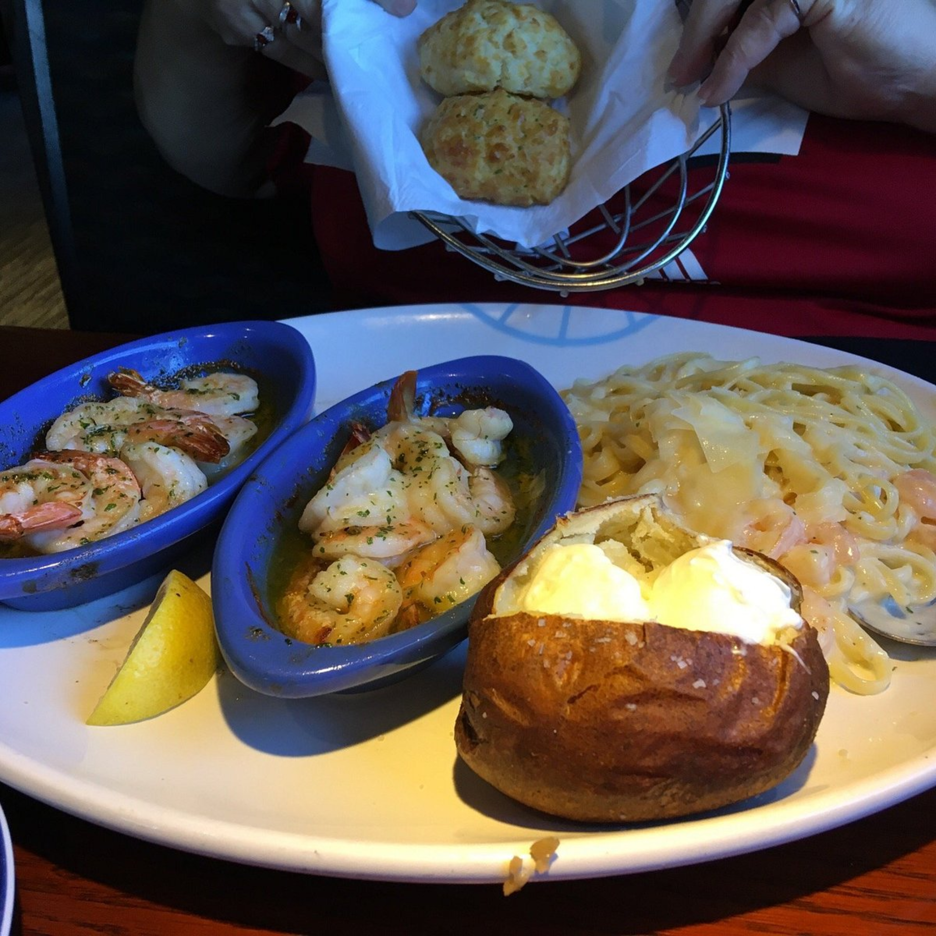 Plate with shrimp in garlic butter, fettuccine, baked potato, and biscuits