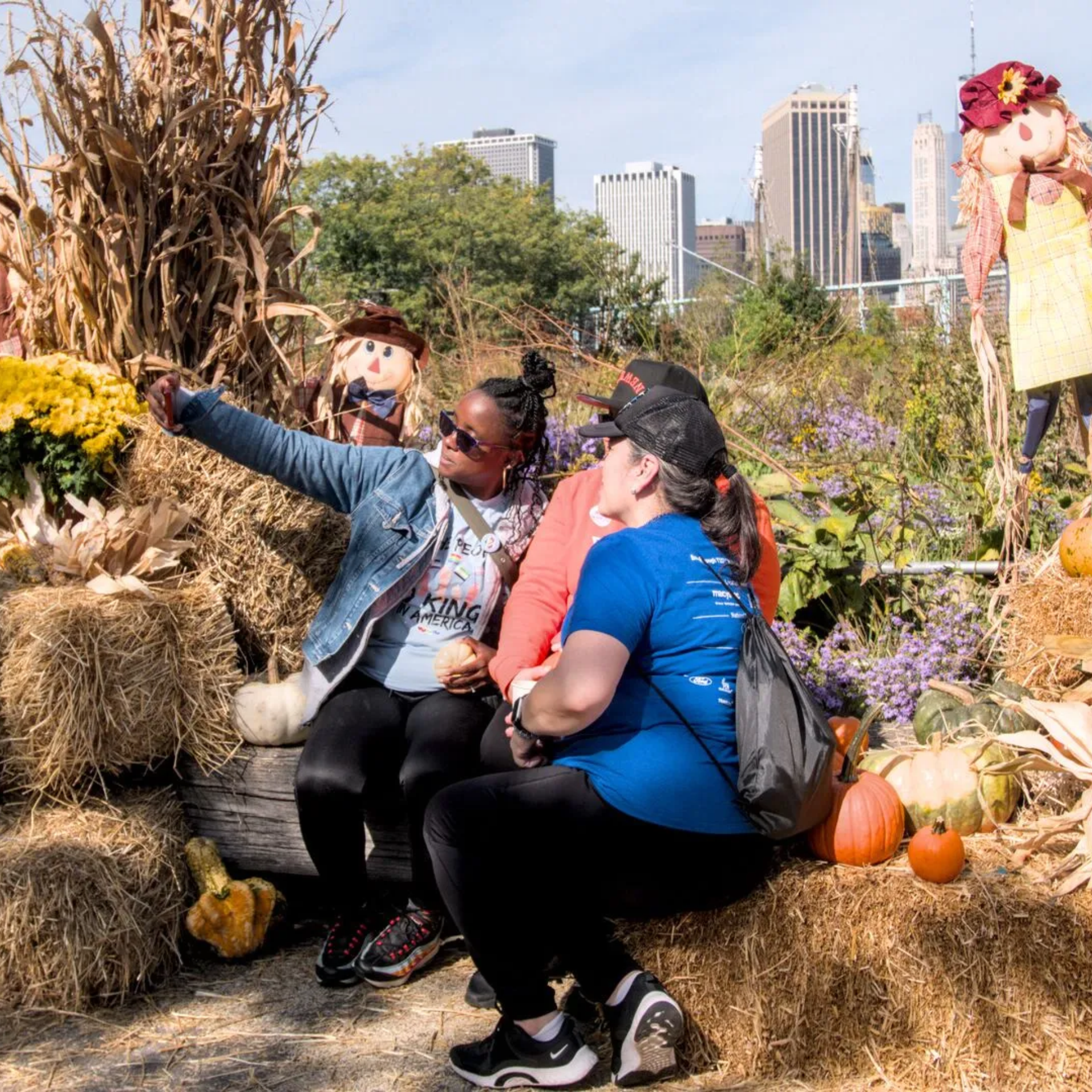 Three people taking selfie on hay bale with pumpkins and scarecrows