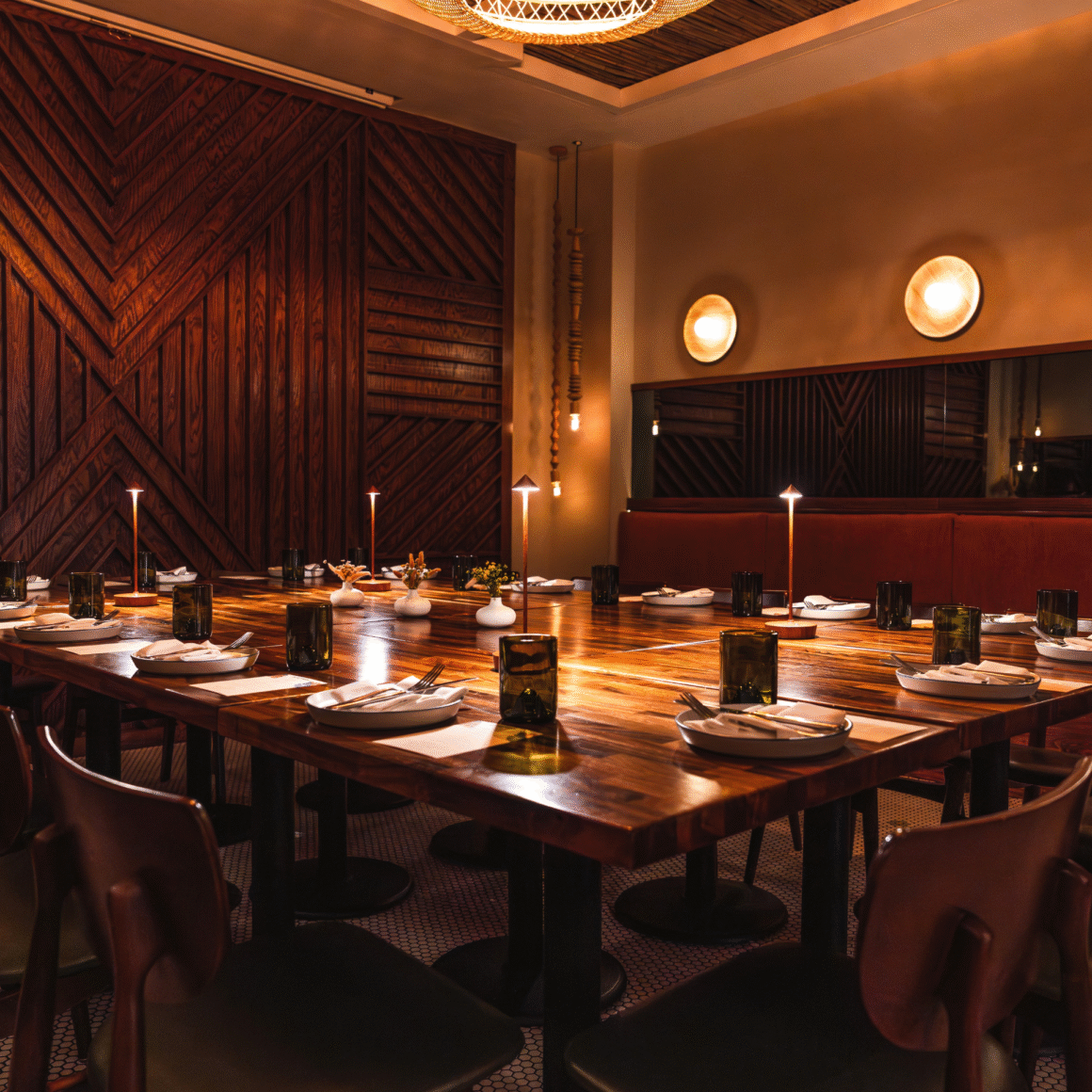 Warmly lit dining room with a U-shaped wooden table, brown chairs, candles, and chevron wood paneling