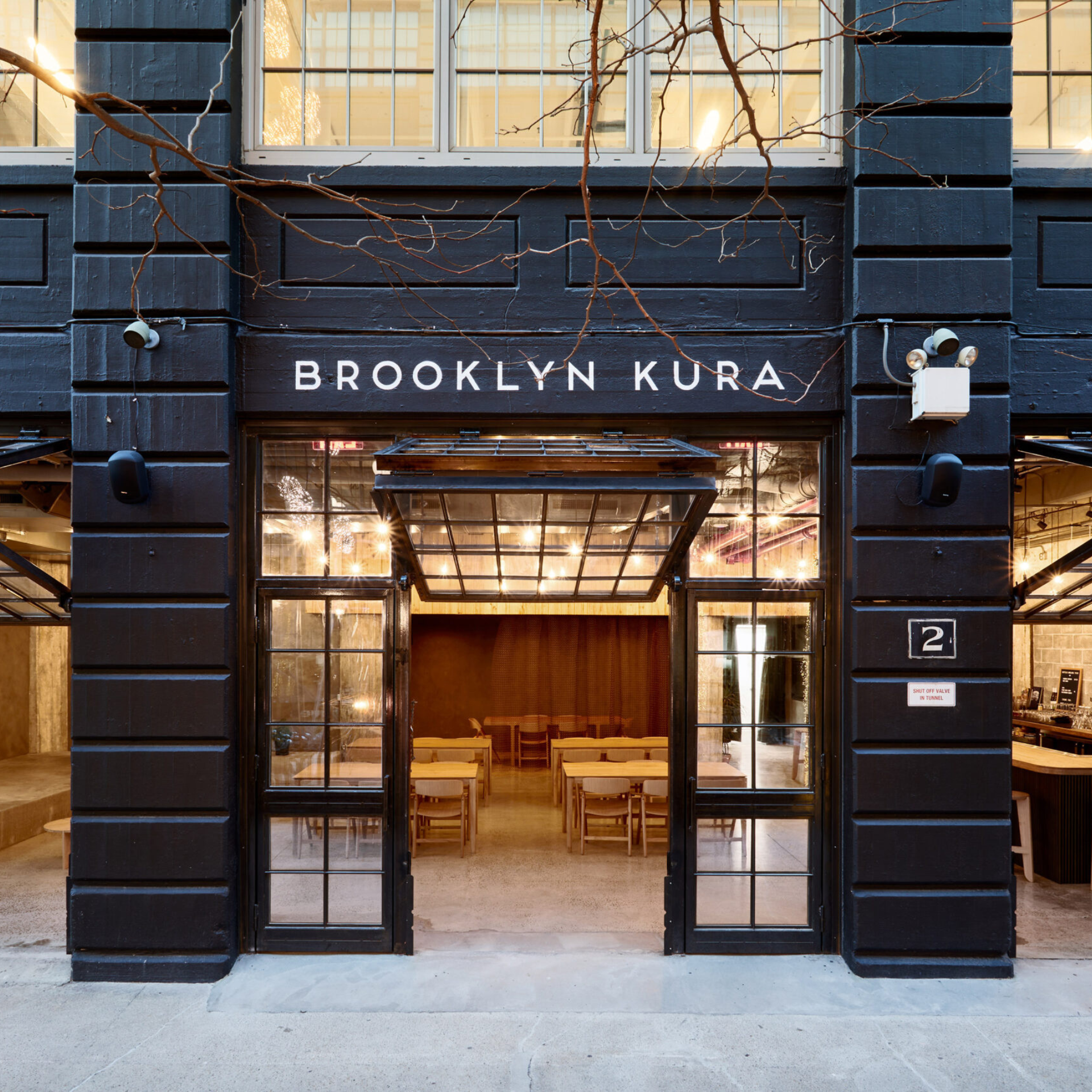 Exterior of Brooklyn Kura with open glass doors and warm interior lighting visible from the street