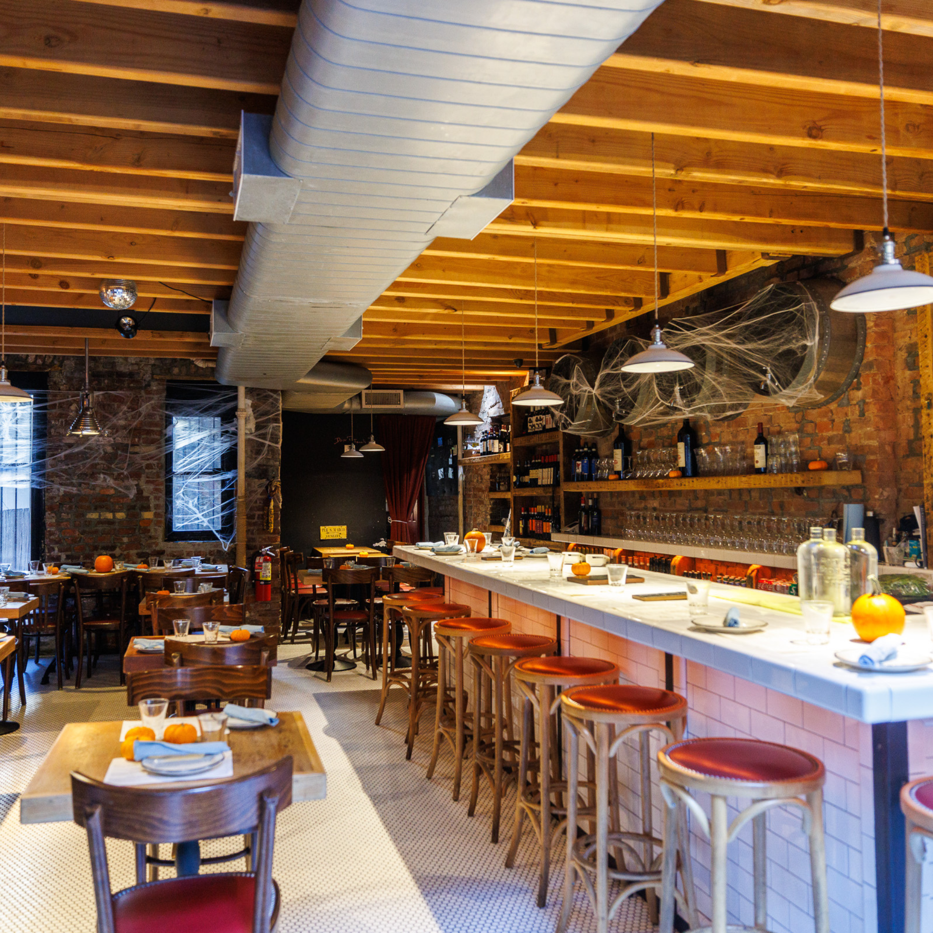 Cozy bar with exposed brick, festive cobwebs, and pumpkins decorating tables for Halloween