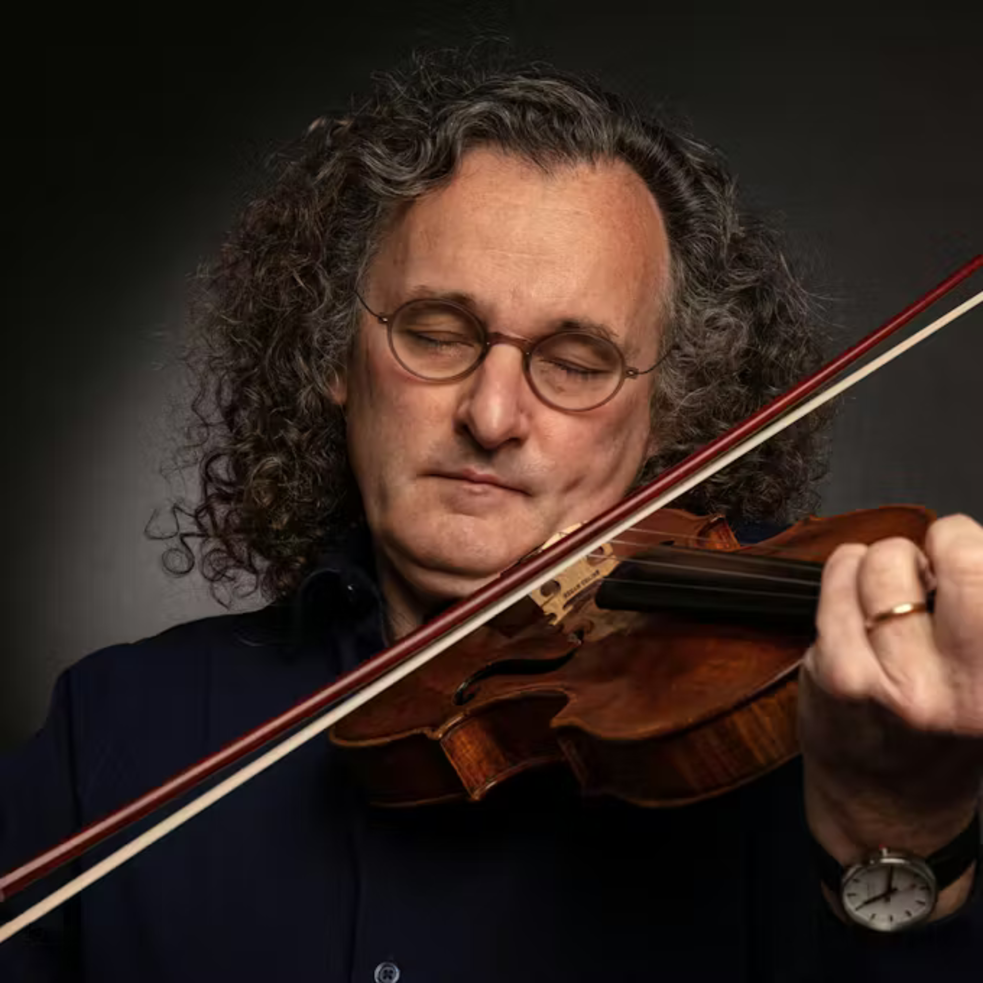 St. Patrick's Day in NYC: Person with gray curly hair playing violin against a dark background