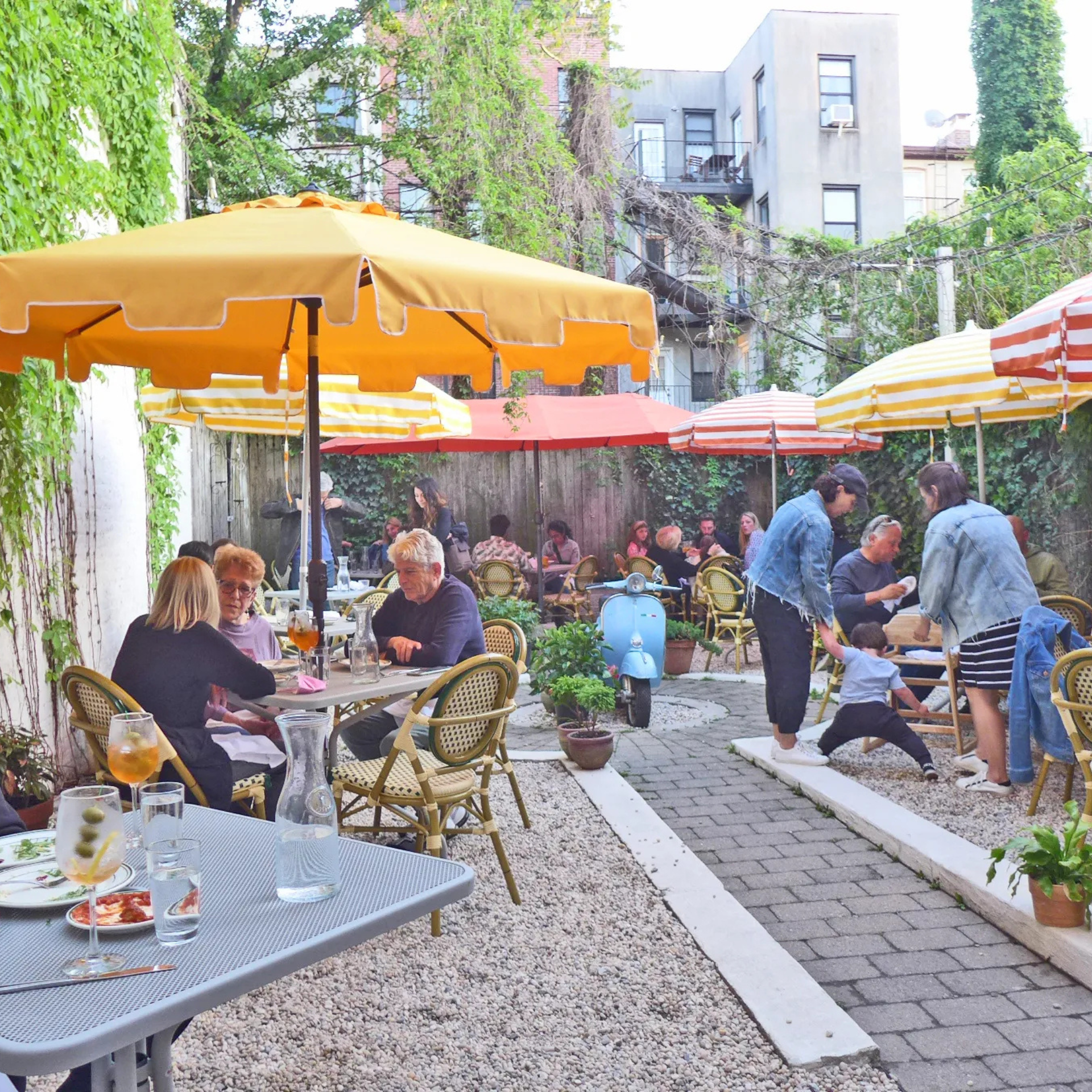 People dining under colorful umbrellas in cozy courtyard café