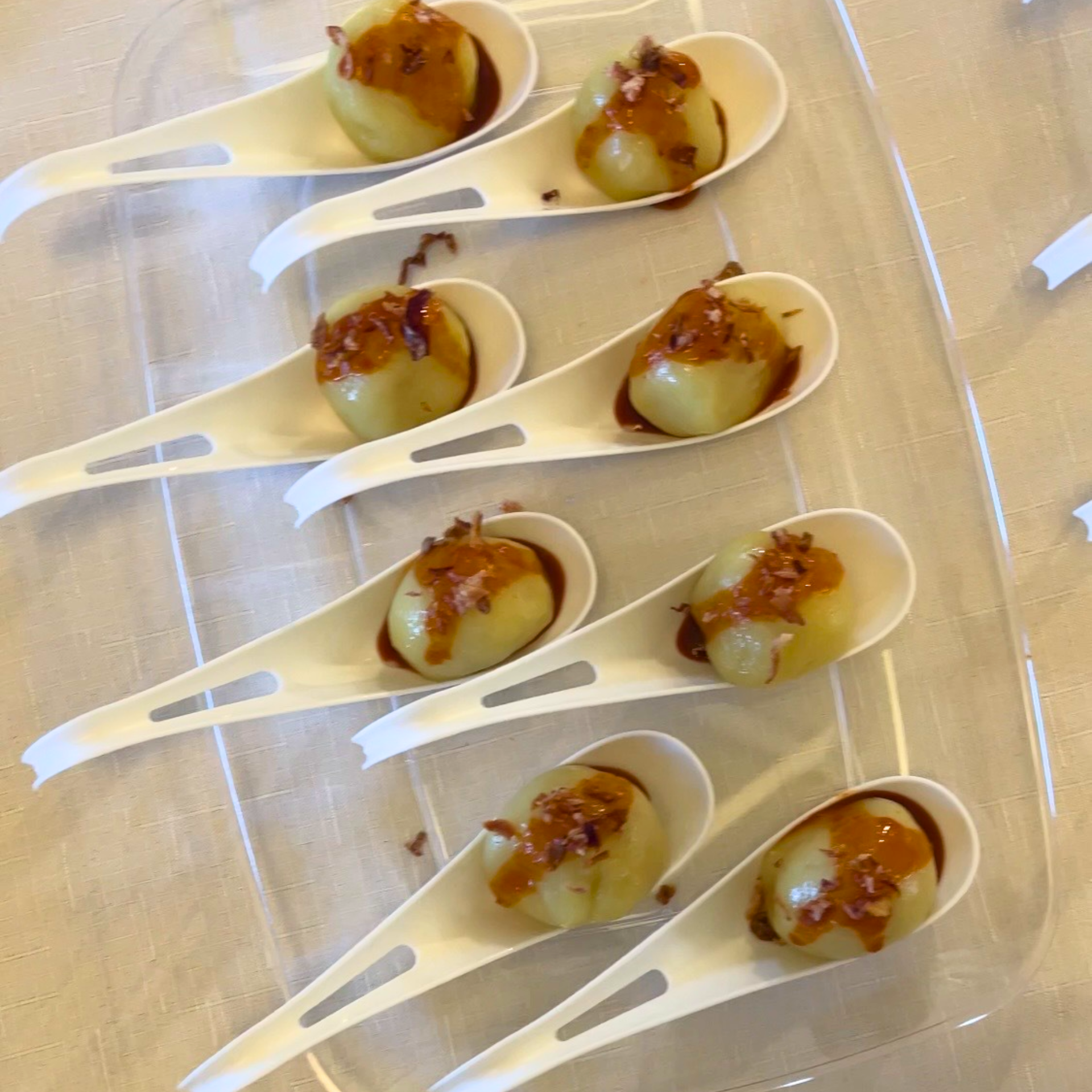 Rows of white serving spoons holding bite‑sized appetizers topped with brown sauce and garnish