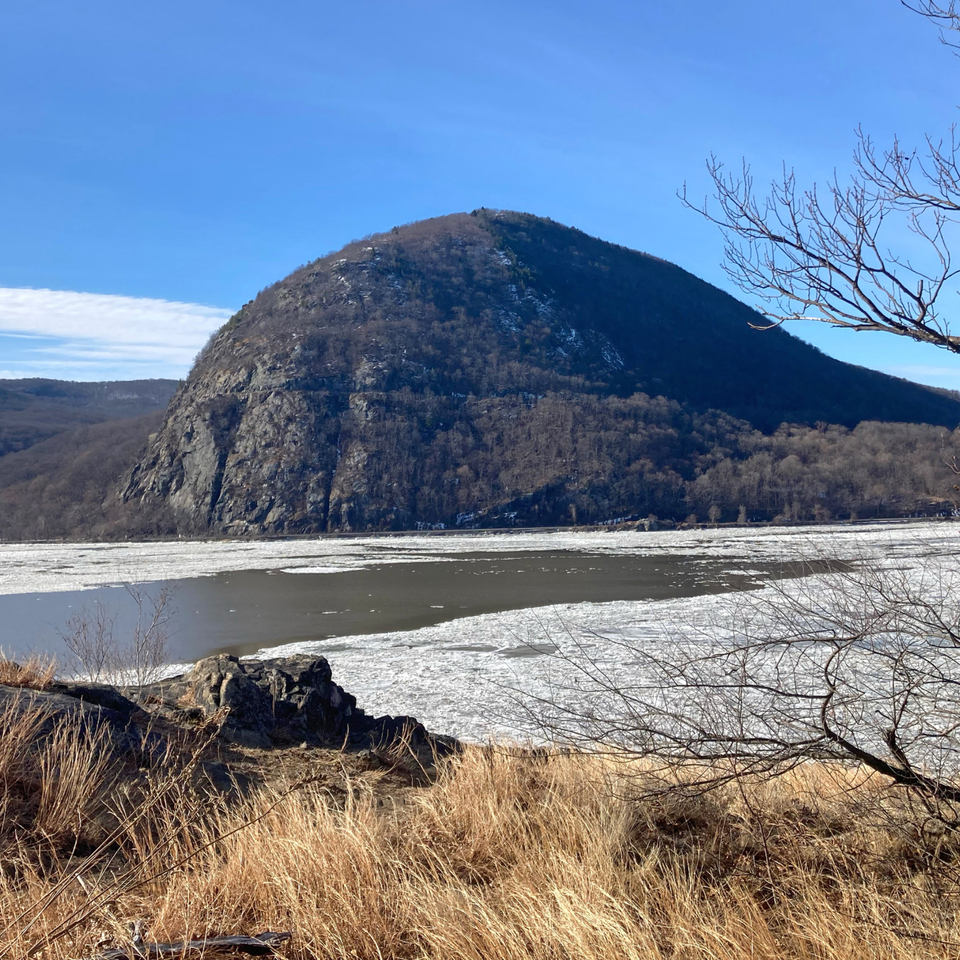 Rounded mountain beside partially frozen river on sunny day