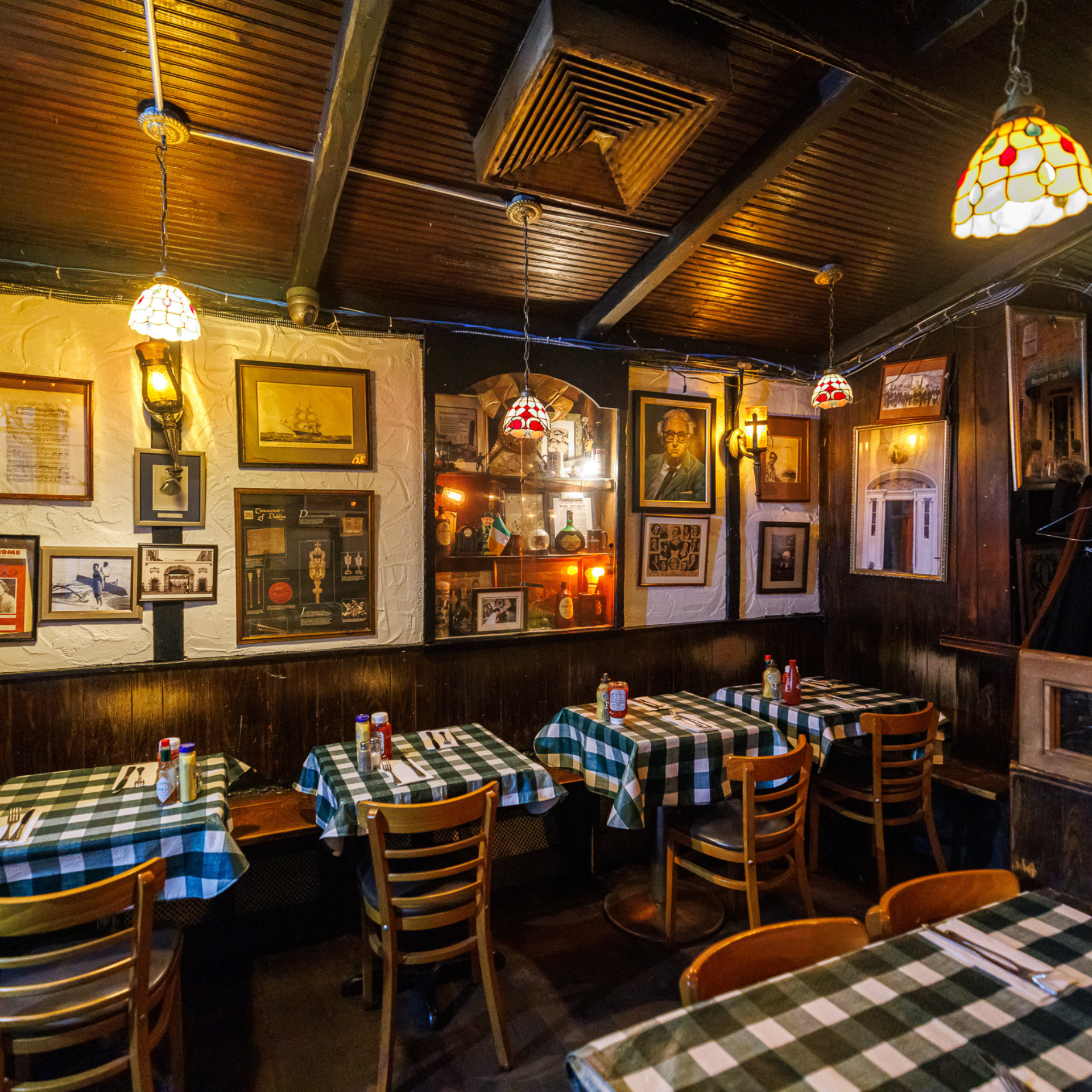 Cozy restaurant interior with checkered tablecloths, stained-glass lights, and walls filled with framed photos and memorabilia