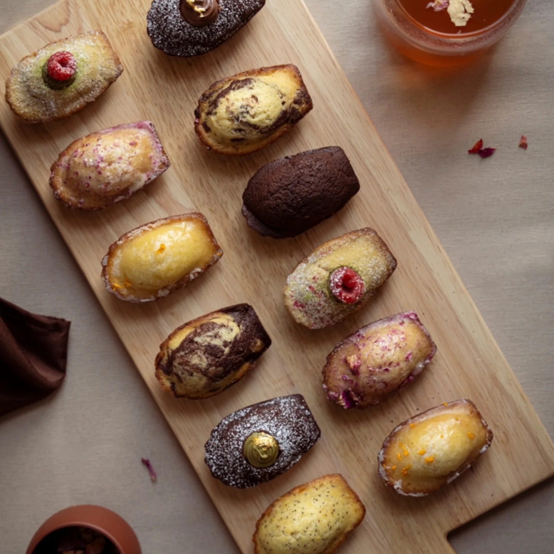 Wooden board with assorted madeleines in different flavors beside a glass of tea