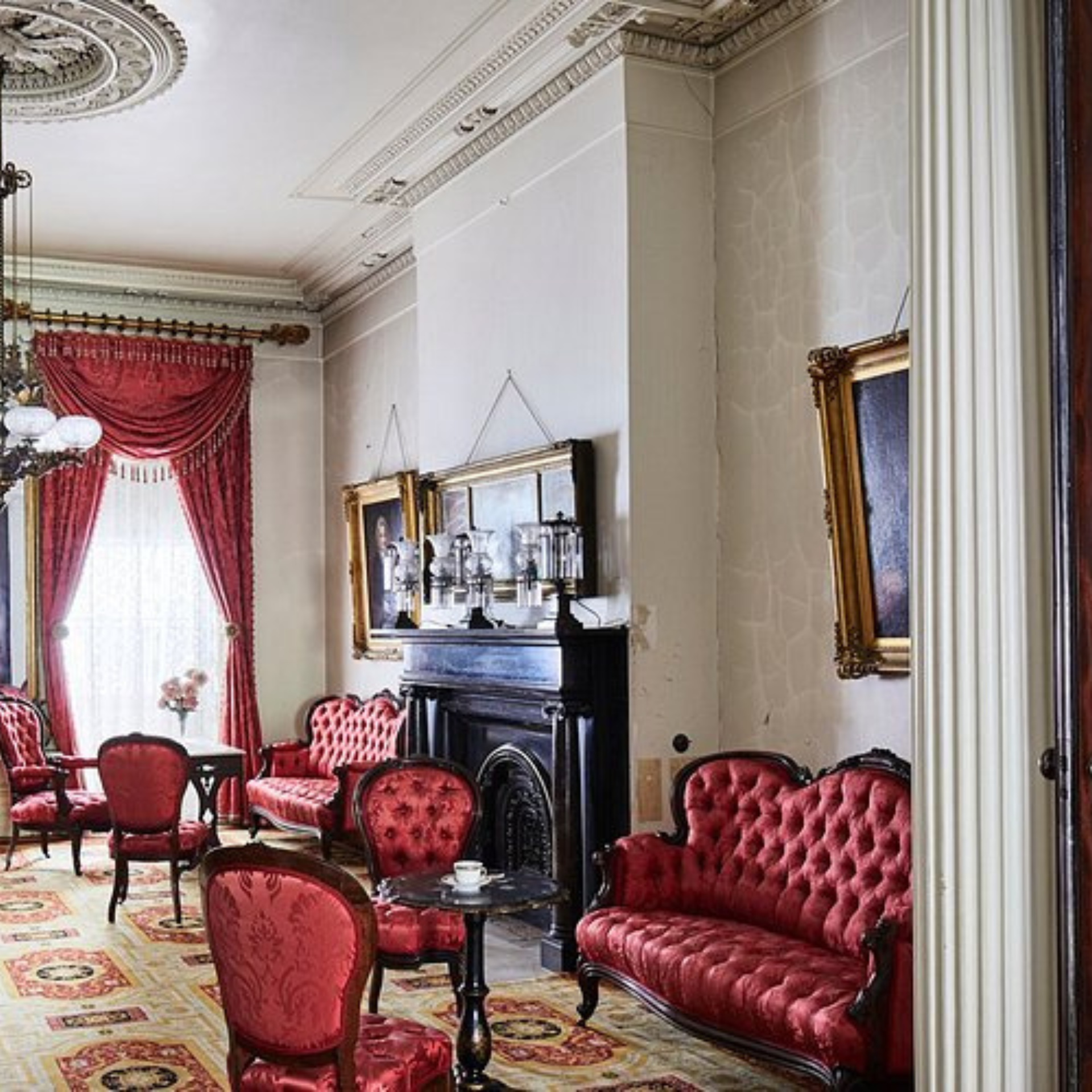 Vintage parlor with red tufted furniture, chandelier, and ornate fireplace