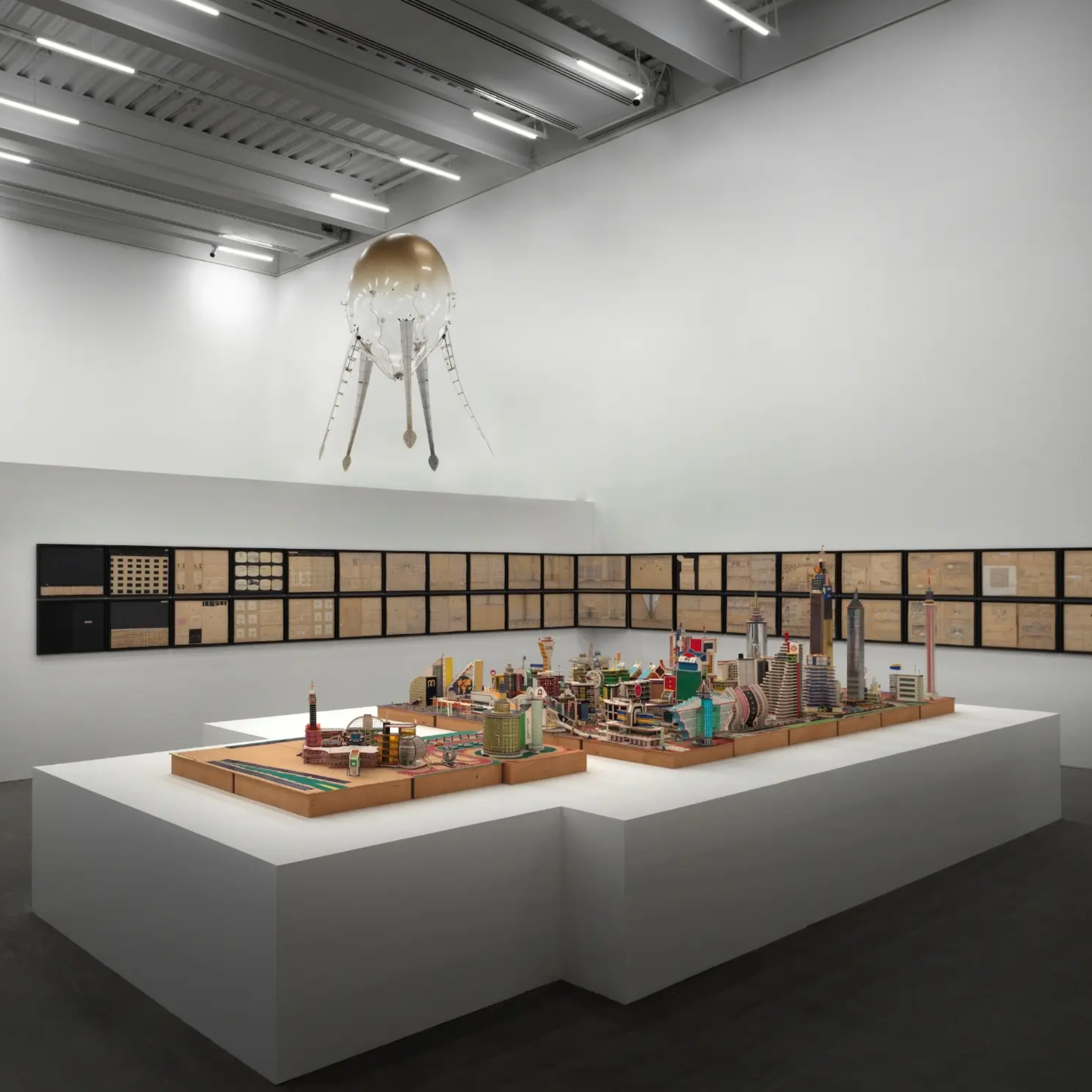 Intricate city model with colorful buildings and futuristic satellite sculpture in gallery
