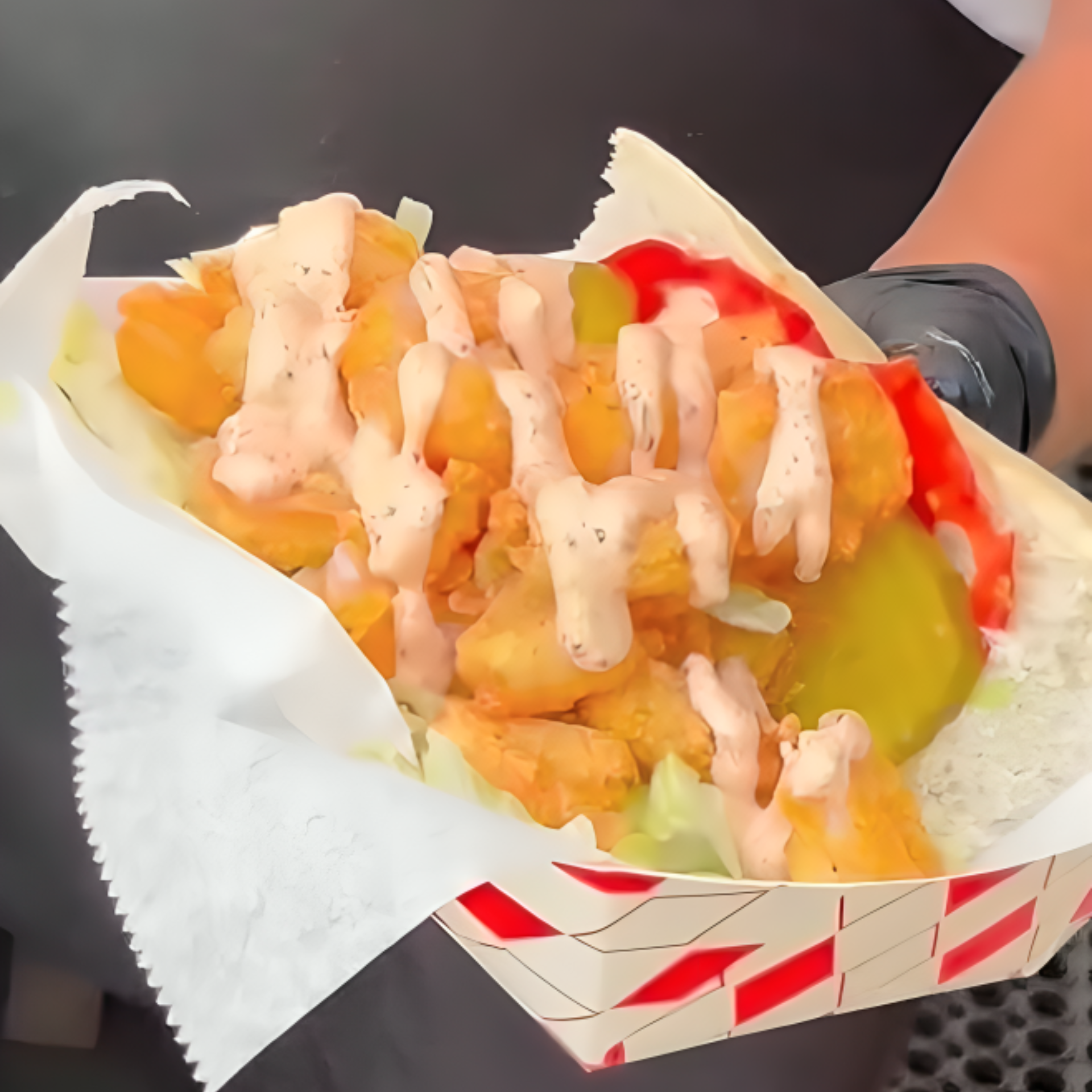 Hand holding a tray with a fried chicken wrap topped with lettuce, pickles, and creamy sauces
