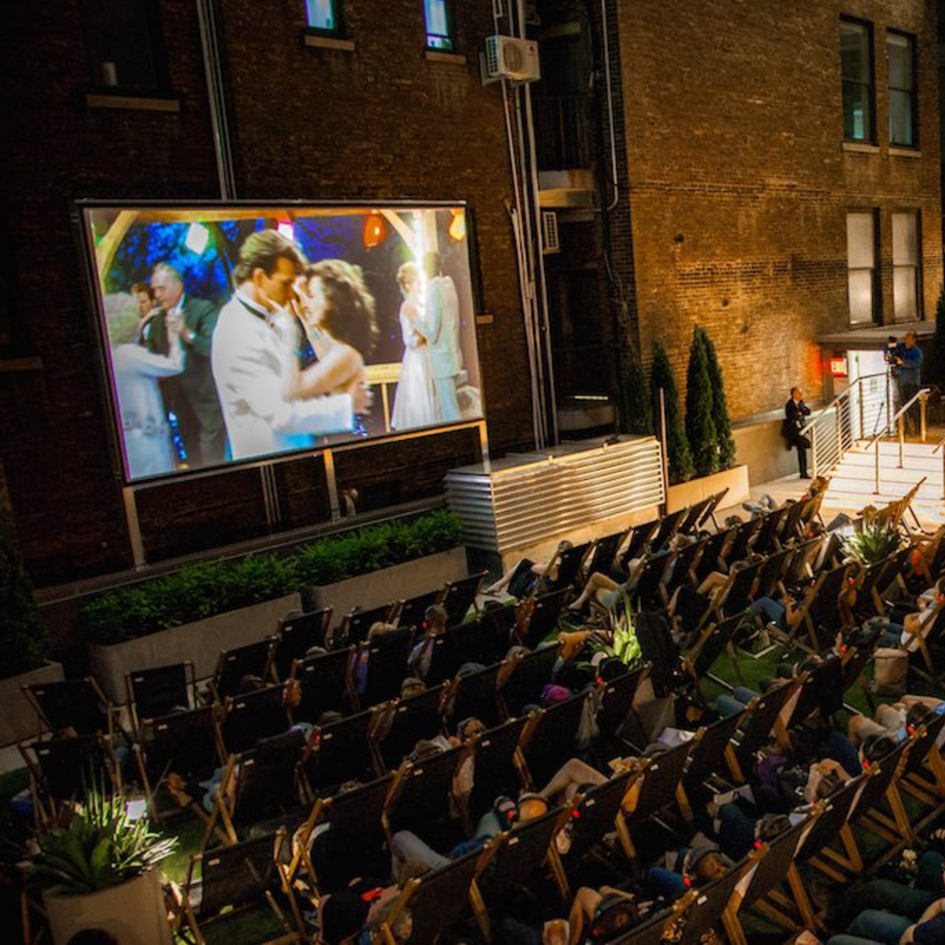 Audience in reclining chairs watching outdoor film in cozy urban courtyard