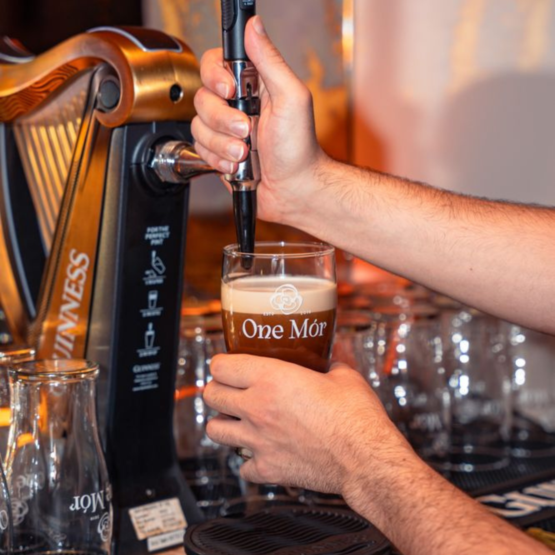 Bartender pouring a pint of Guinness into a branded One Mór glass at the bar