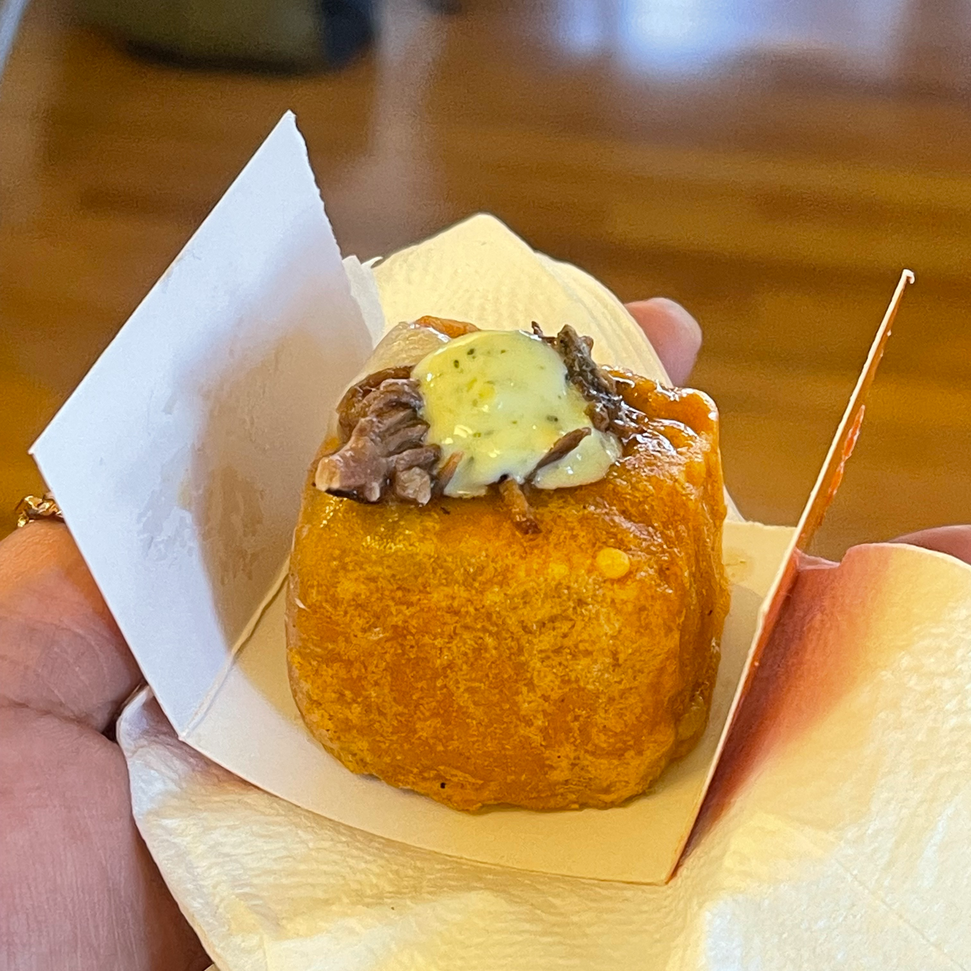 Hand holding a crispy fried cube topped with shredded meat and creamy sauce