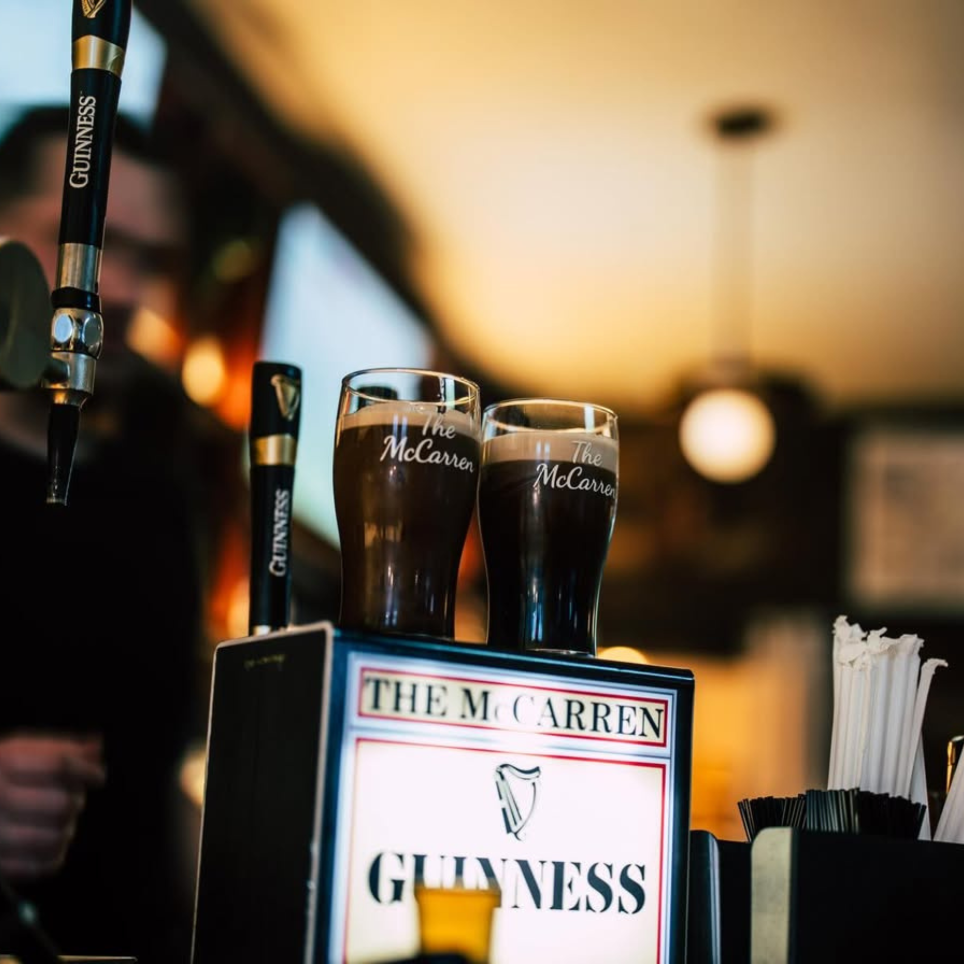 Two pints of Guinness on a bar counter at The McCarren, with branded taps and dispenser in the background