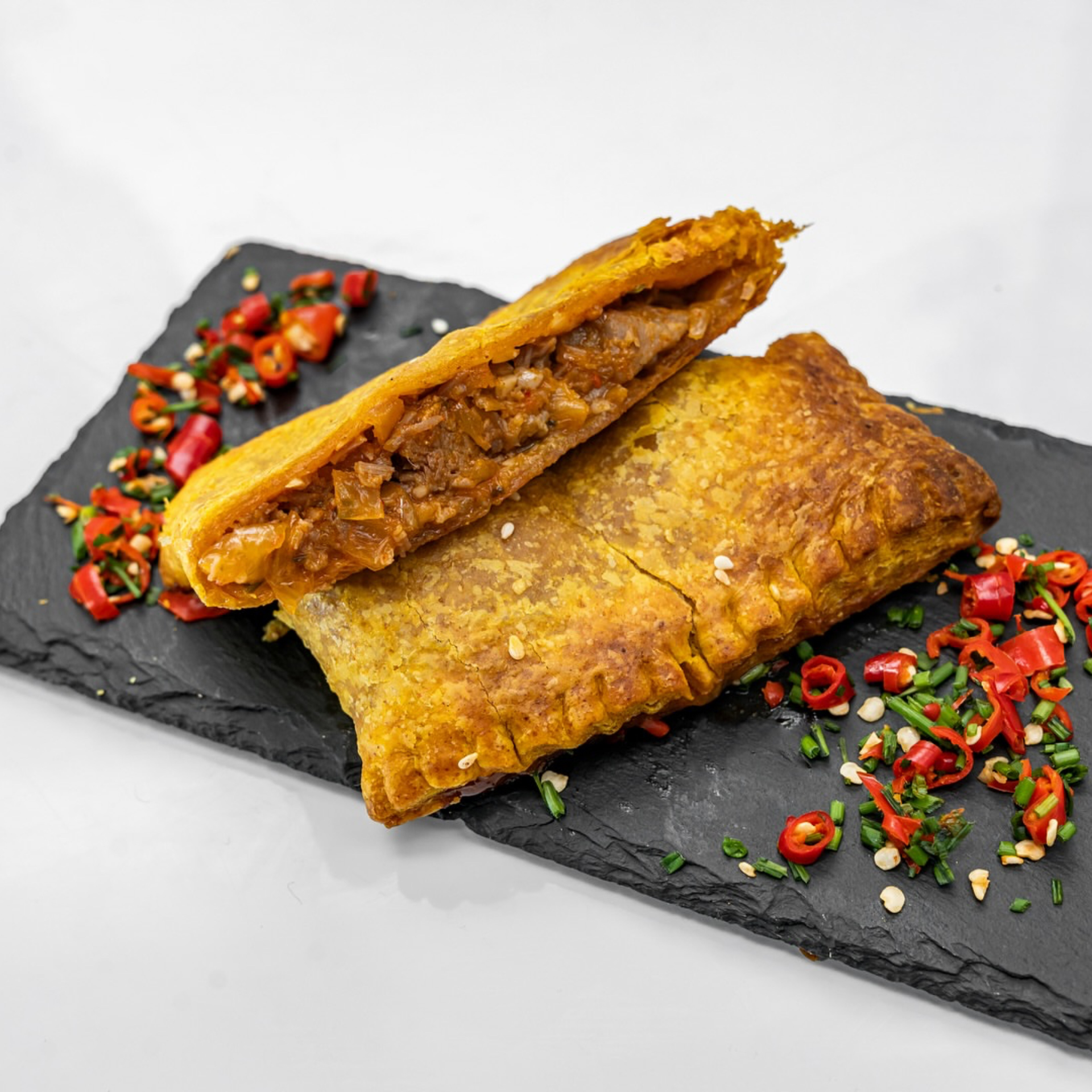 Smorgasburg NYC: Golden flaky pastry cut open to show a meat filling, served on a black slate with chili and herb garnish