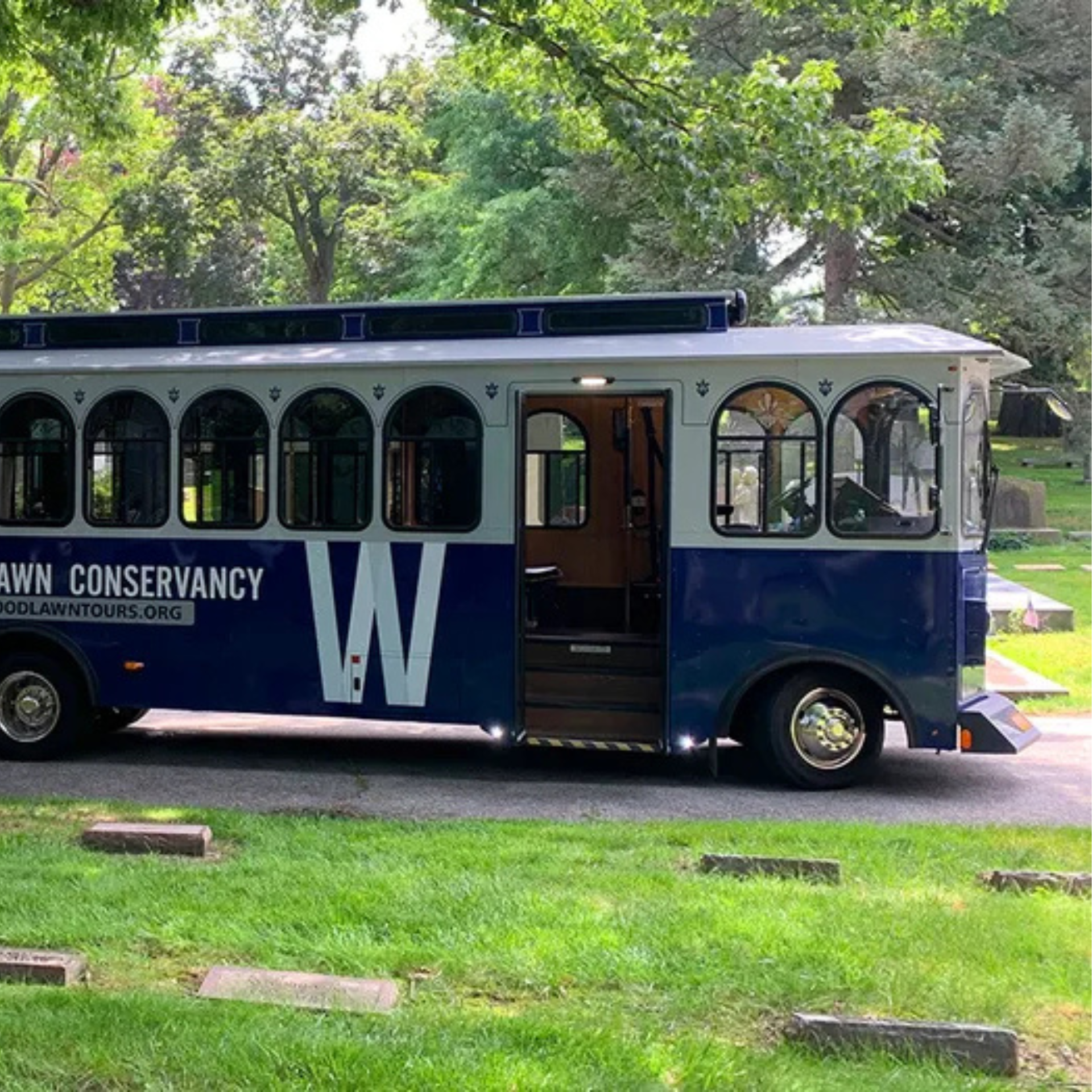 Blue and white Woodlawn Conservancy tour bus parked in a cemetery